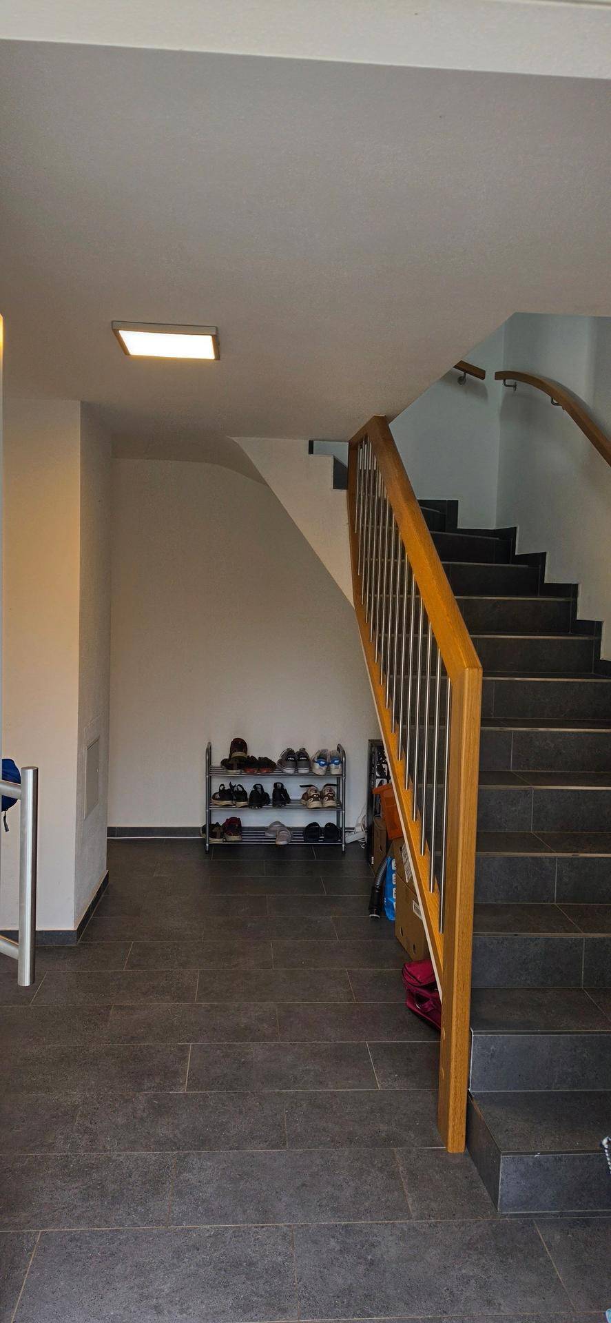 Heller Eingangsbereich mit dunklen Fliesen, Holztreppe und Schuhregal.