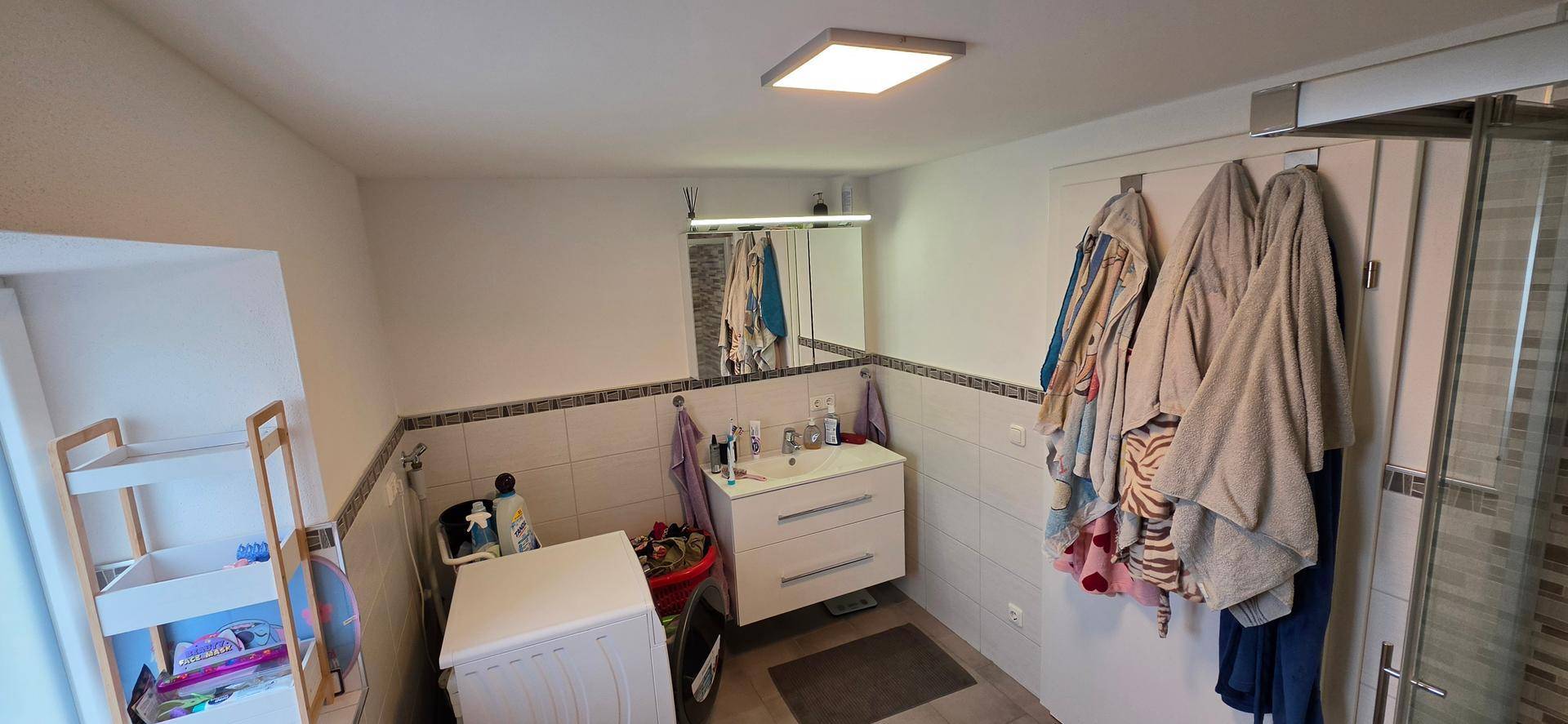 Funktionales Badezimmer mit Waschbecken, Spiegel und Platz für eine Waschmaschine.