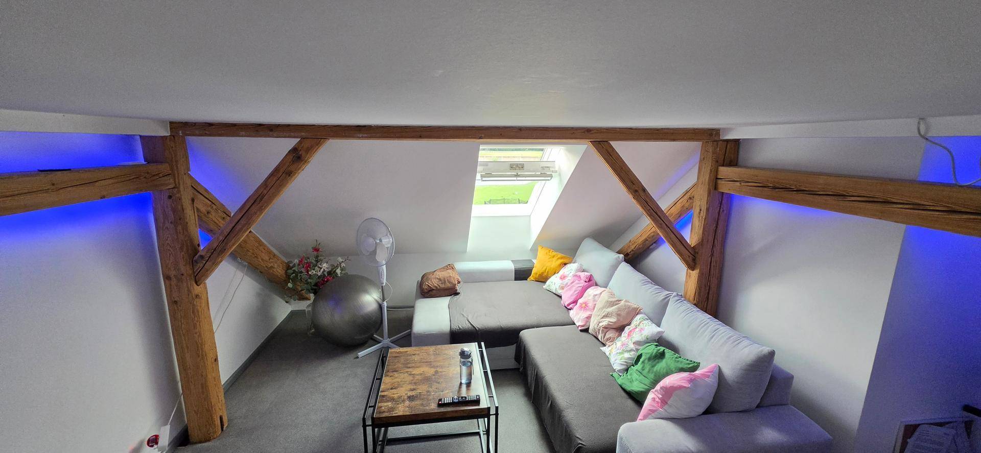 Helles Dachgeschoss-Wohnzimmer mit bequemer Couch, Holzbalken und farbigen Akzenten.