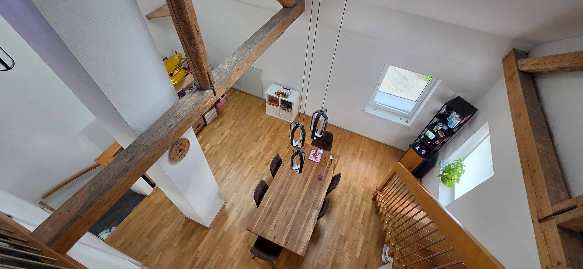 Blick von oben auf den offenen Wohn-Essbereich mit Holztisch und Treppe.