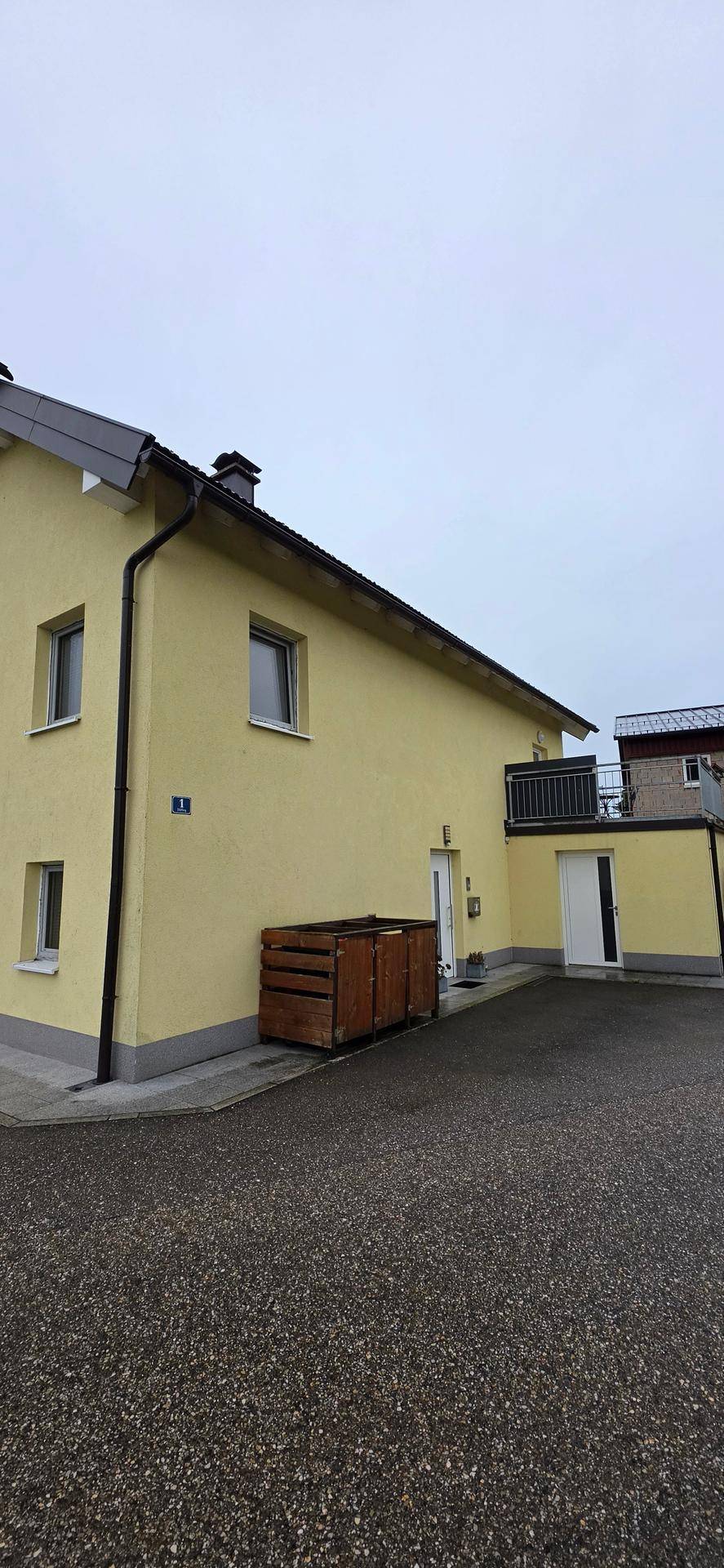 Seitenansicht des gelben Hauses mit Fenstern und einem kleinen Balkon.