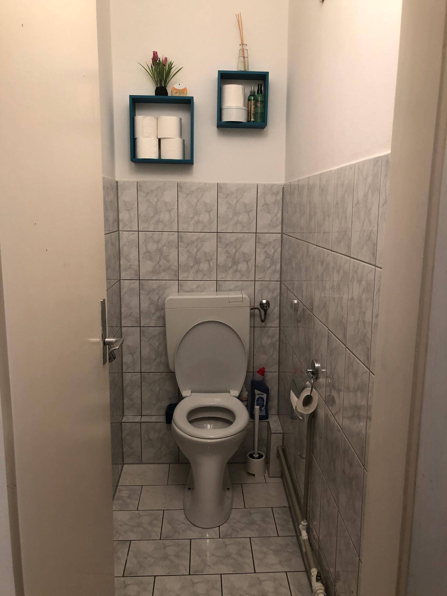 Separate Toilette mit Fliesen an den Wänden und praktischen Wandregalen.
