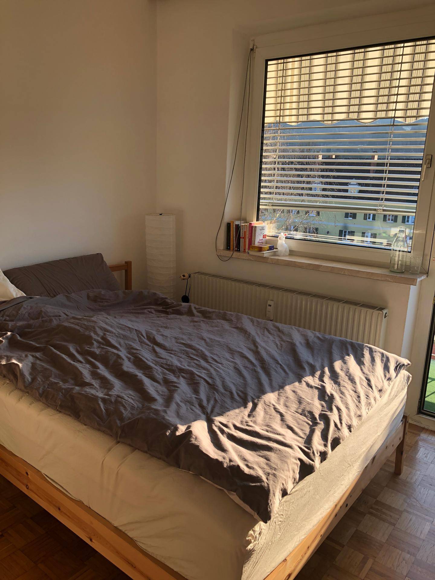 Schlafzimmer mit Holzbett, Parkettboden und viel natürlichem Licht durch das Fenster.