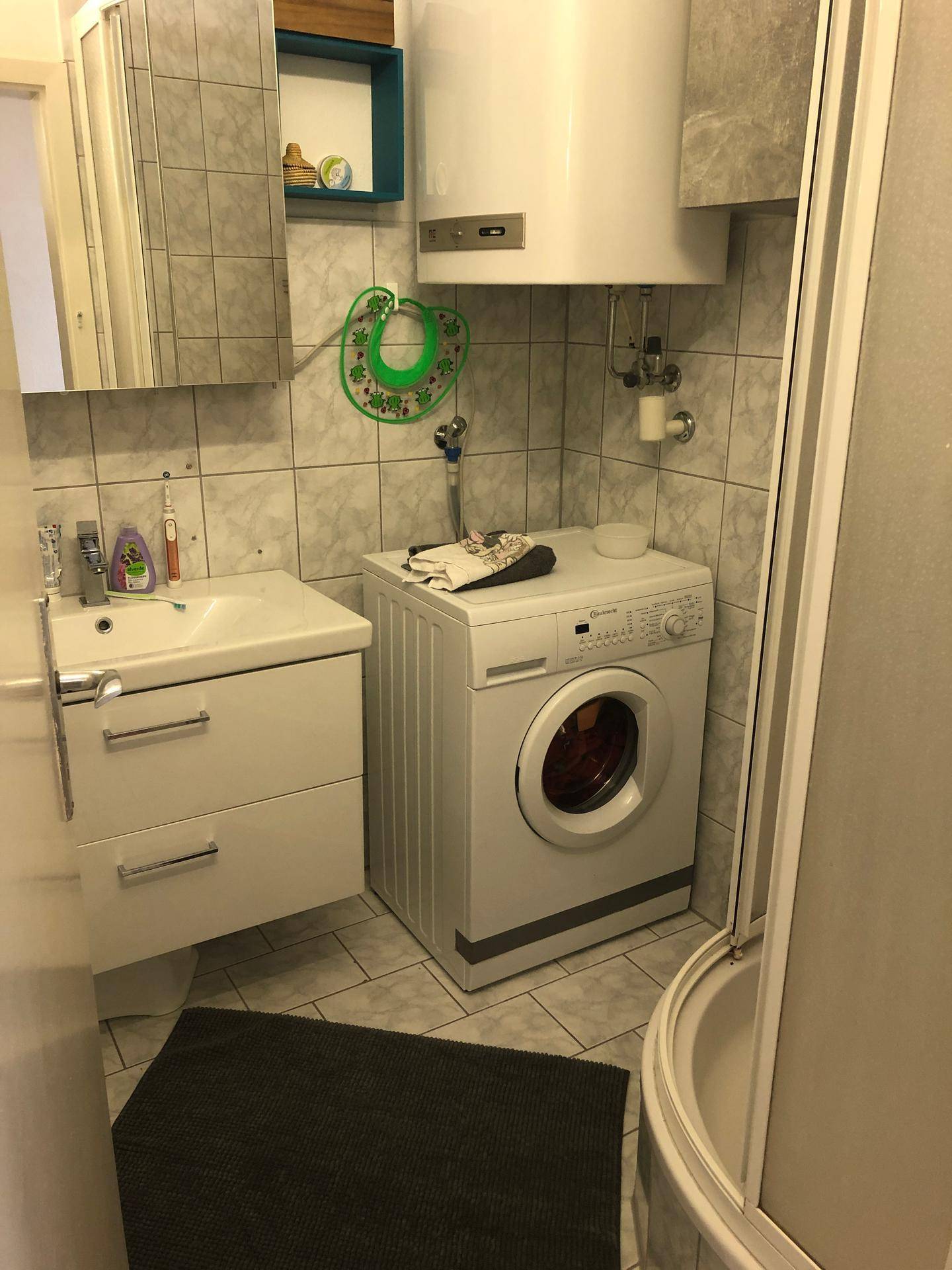 Badezimmer mit Dusche, Waschbecken und integrierter Waschmaschine.