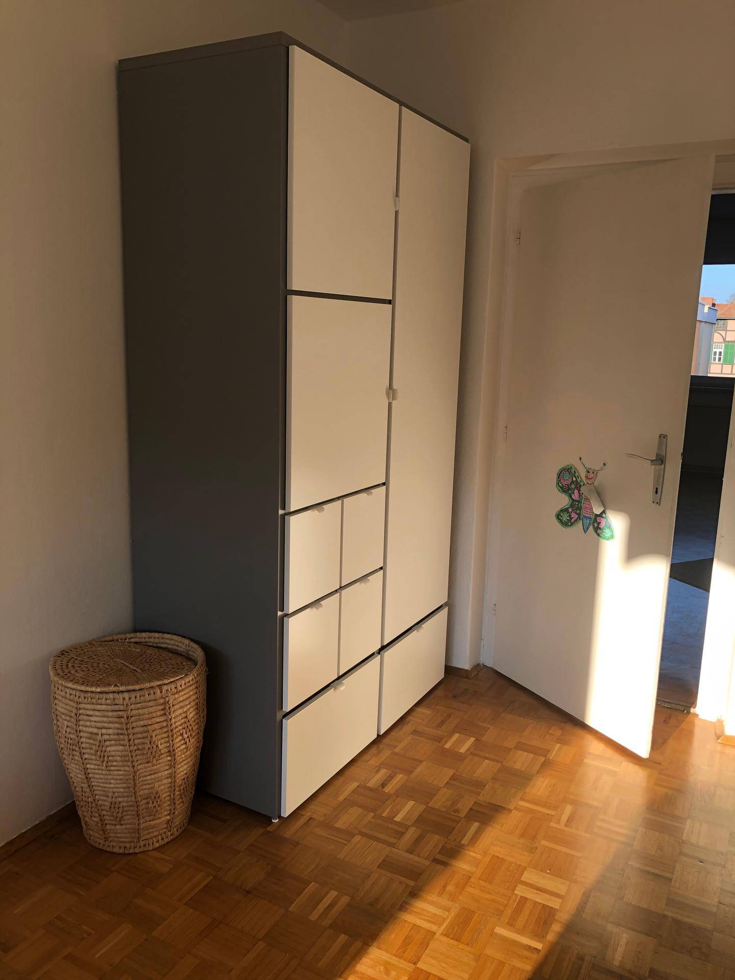 Geräumiger Kleiderschrank mit hellen Fronten und Parkettboden in einem Schlafzimmer.