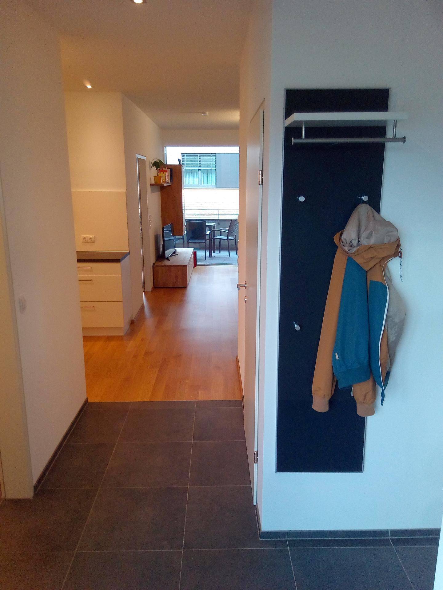 Heller Flur mit dunklen Fliesen und Garderobe, der zum Wohnbereich führt.