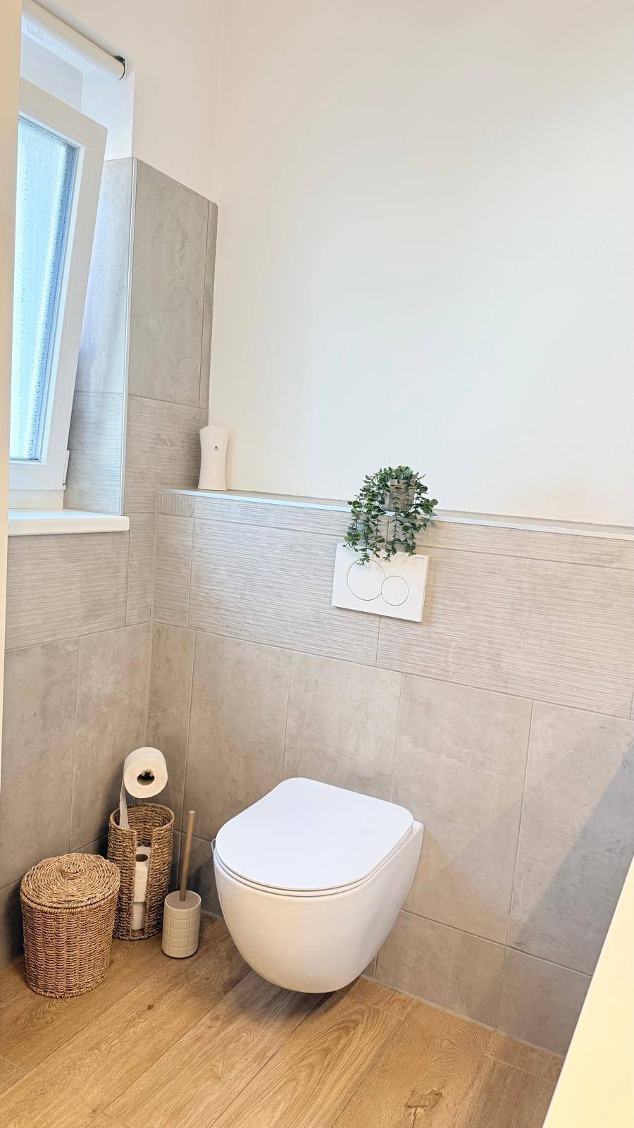 WC mit wandhängender Toilette, modernen Fliesen und einem Fenster für Tageslicht.