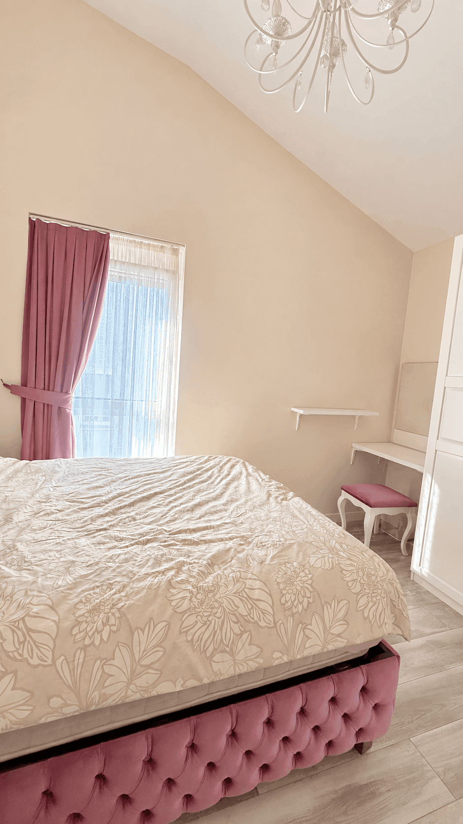 Schlafzimmer mit großem Bett, Schminktisch und Fenster mit Vorhängen unter einer Dachschräge.