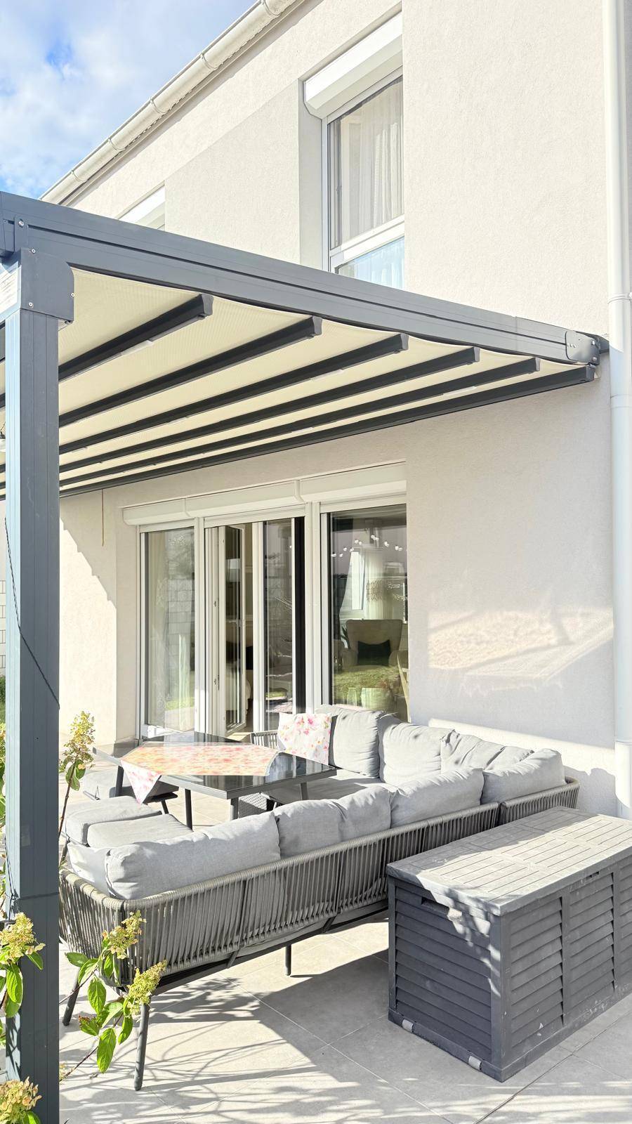Überdachte Terrasse mit Pergola, bequemen Gartenmöbeln und einer praktischen Aufbewahrungsbox.