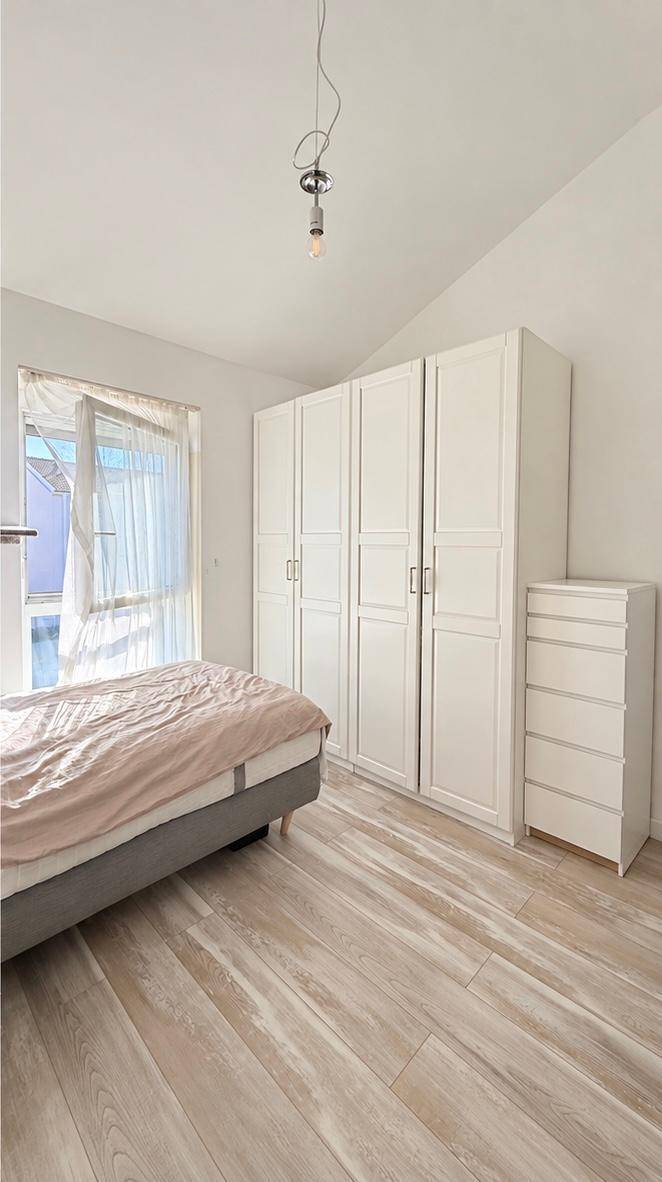 Helles Schlafzimmer mit großem weißen Kleiderschrank und Fenster unter einer Dachschräge.