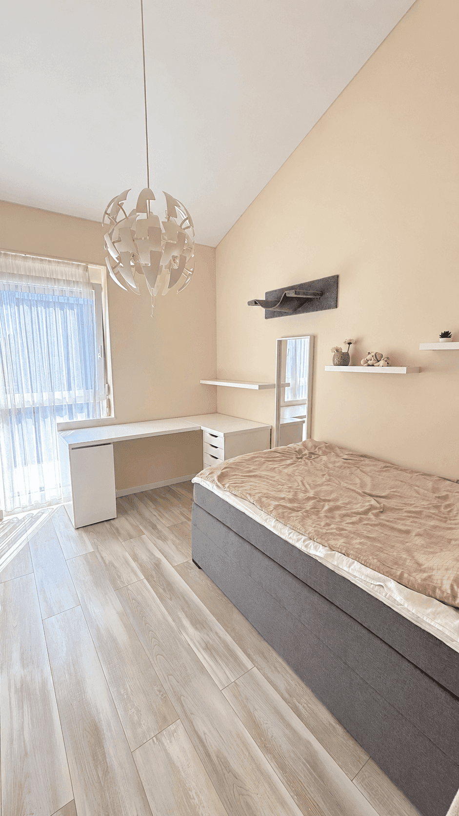 Helles Zimmer mit Einzelbett, Schreibtisch und Fenster unter einer Dachschräge.
