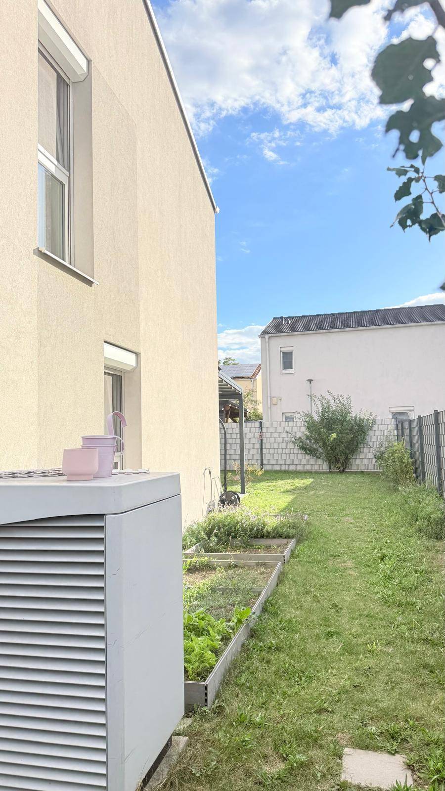 Seitlicher Gartenbereich mit Hochbeeten für den Anbau von Gemüse und einer Wärmepumpe.