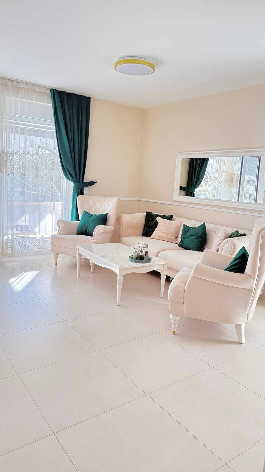 Helles Wohnzimmer mit beigen Sofas, Couchtisch und großen Fenstern zum Garten.