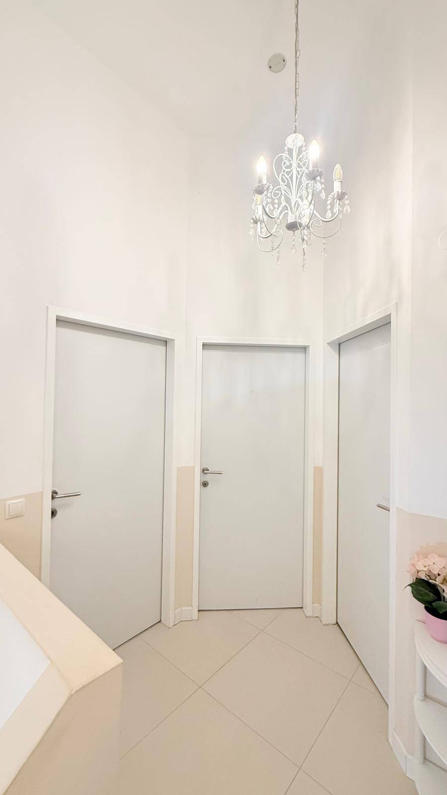 Heller Flur mit mehreren Türen und einem eleganten Kronleuchter an der Decke.