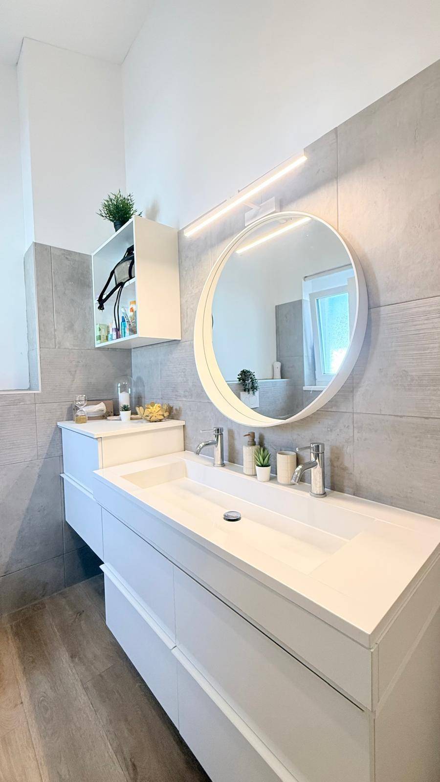 Modernes Badezimmer mit Doppelwaschbecken, rundem Spiegel und eleganten Fliesen.