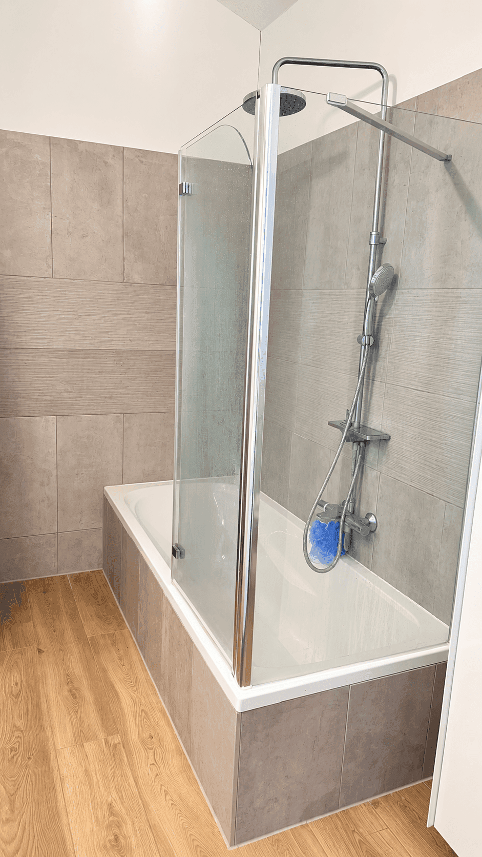Badezimmer mit Badewanne, Duschvorrichtung und modernen Fliesen an den Wänden.