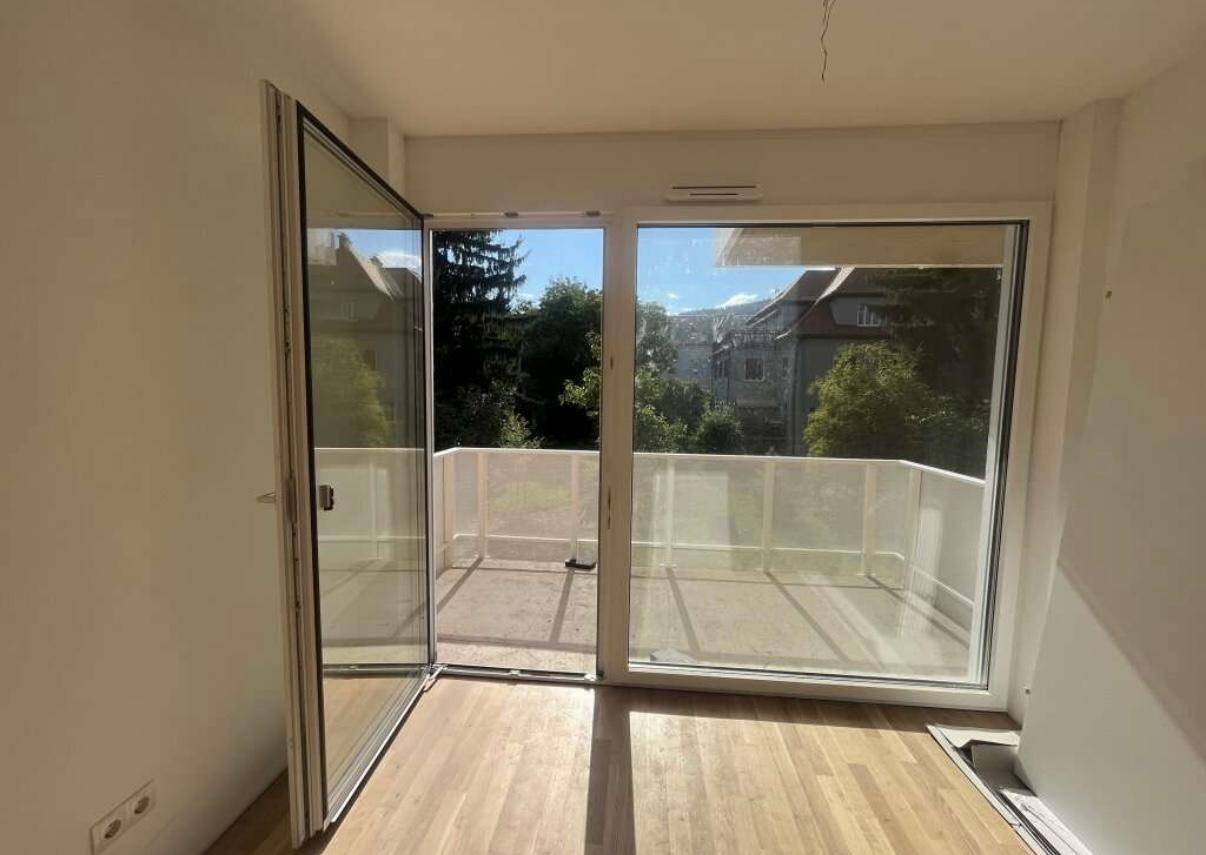 Wohnzimmer mit Holzboden und offener Balkontür, die viel Tageslicht hereinlässt.