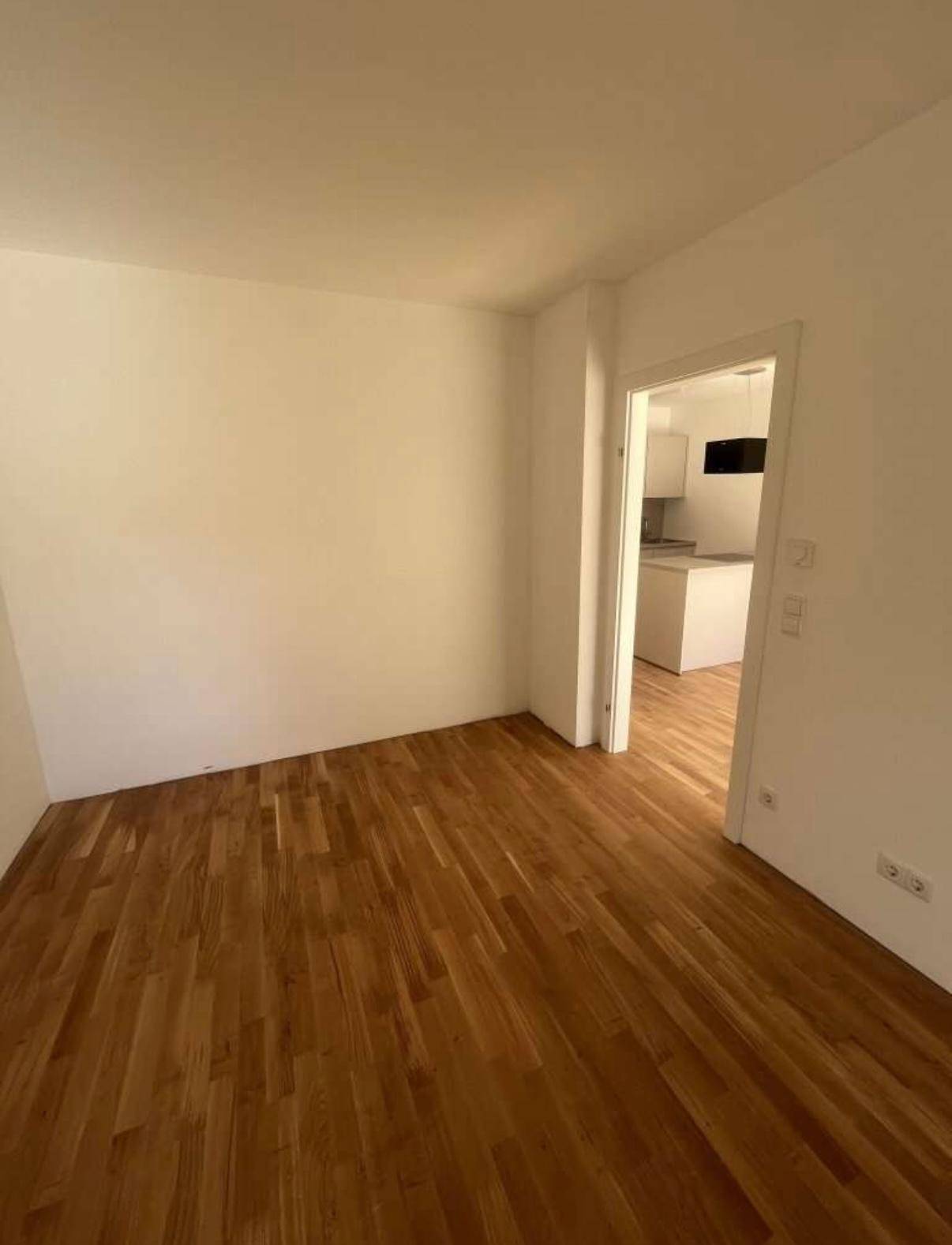 Heller Flur mit Holzboden, der den Blick in die moderne Küche freigibt.