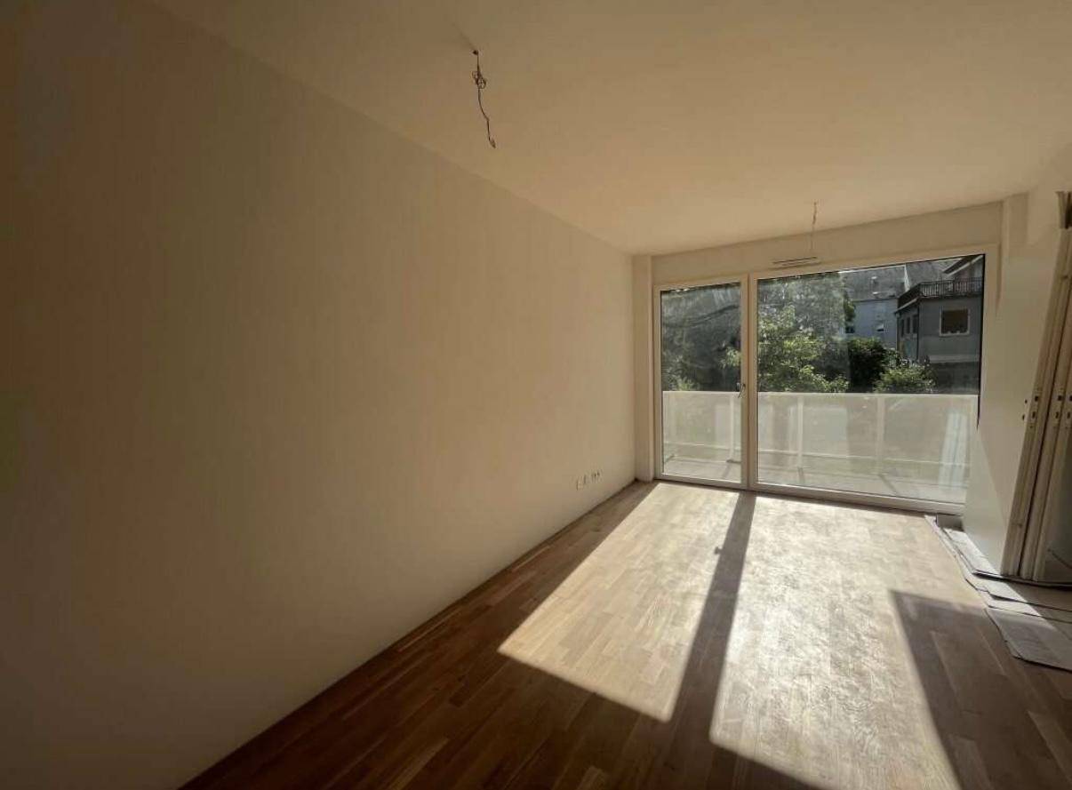 Helles Wohnzimmer mit Holzboden und Zugang zu einem Balkon, durchflutet von Sonnenlicht.