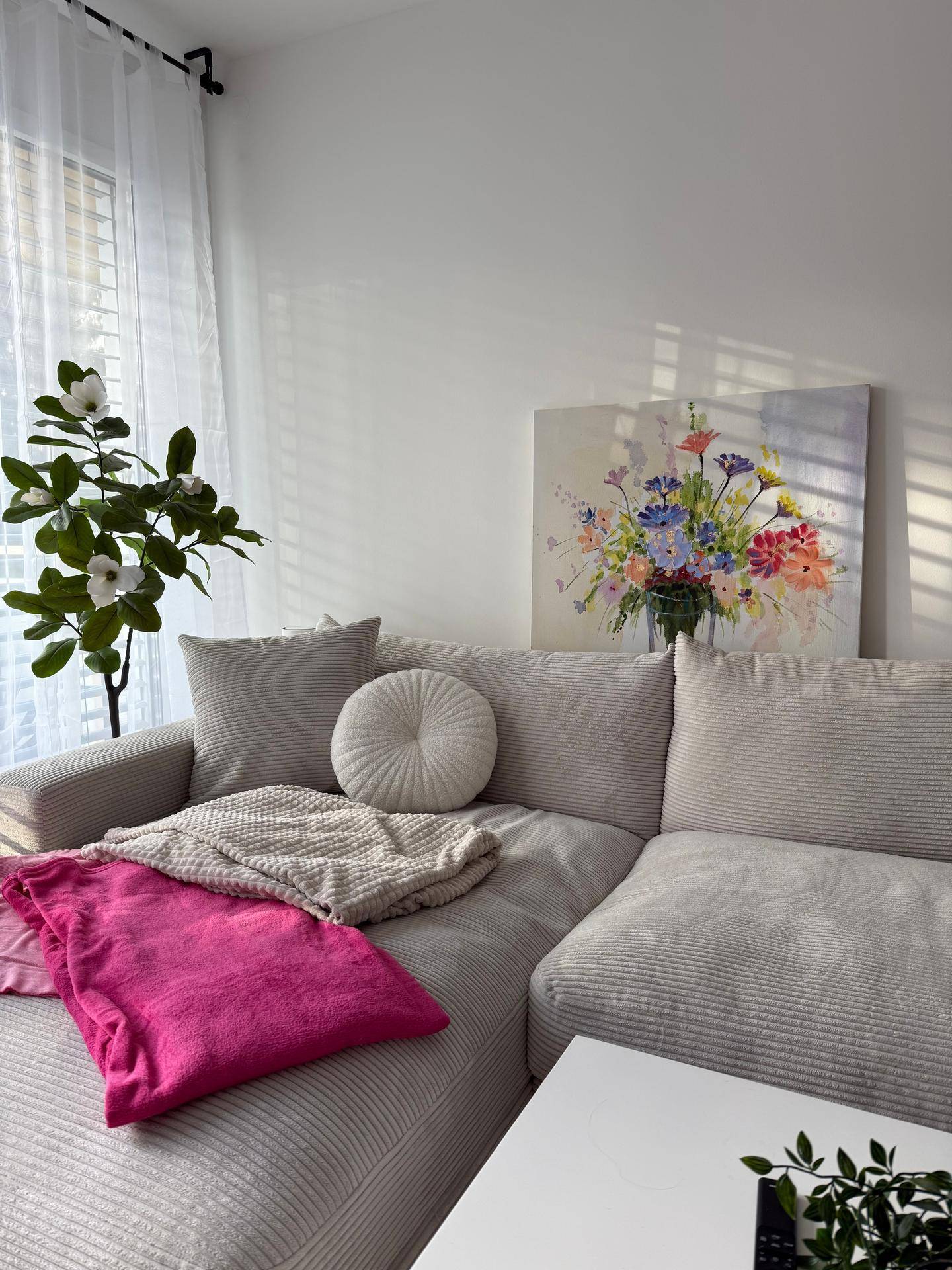 Gemütliches Wohnzimmer mit hellem Sofa, farbenfrohem Gemälde und viel Tageslicht.