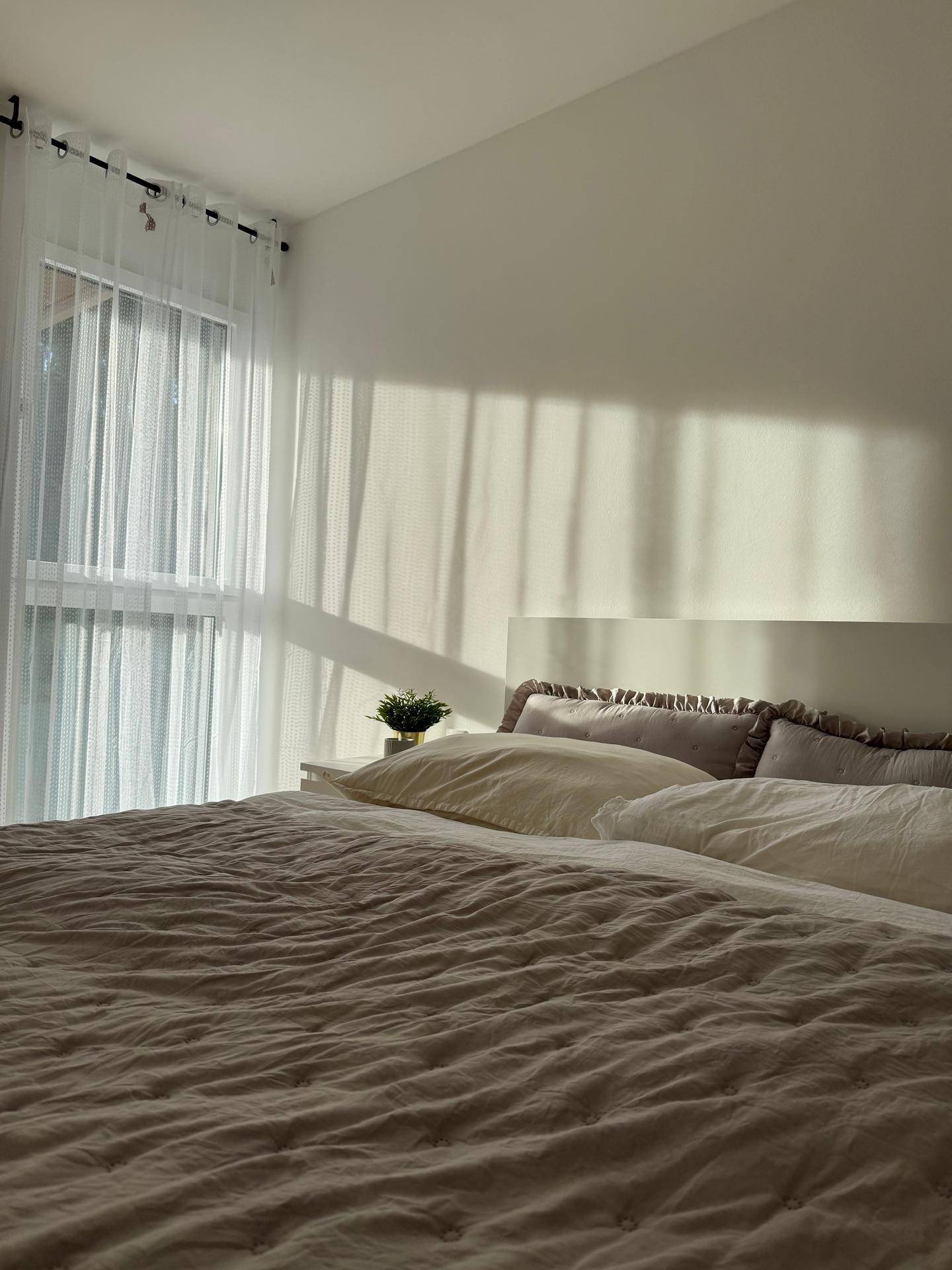 Helles Schlafzimmer mit Doppelbett, weißen Vorhängen und sanftem Sonnenlicht.