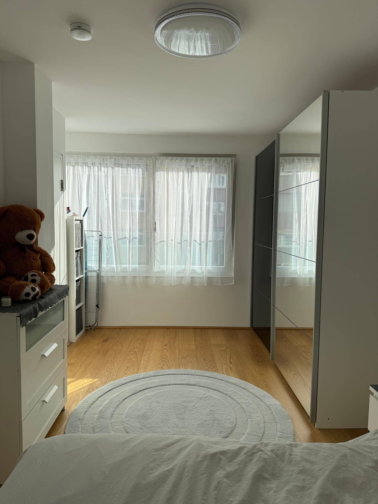 Schlafzimmer mit großen Fenstern, Holzboden und einem Kleiderschrank mit Spiegelfronten.
