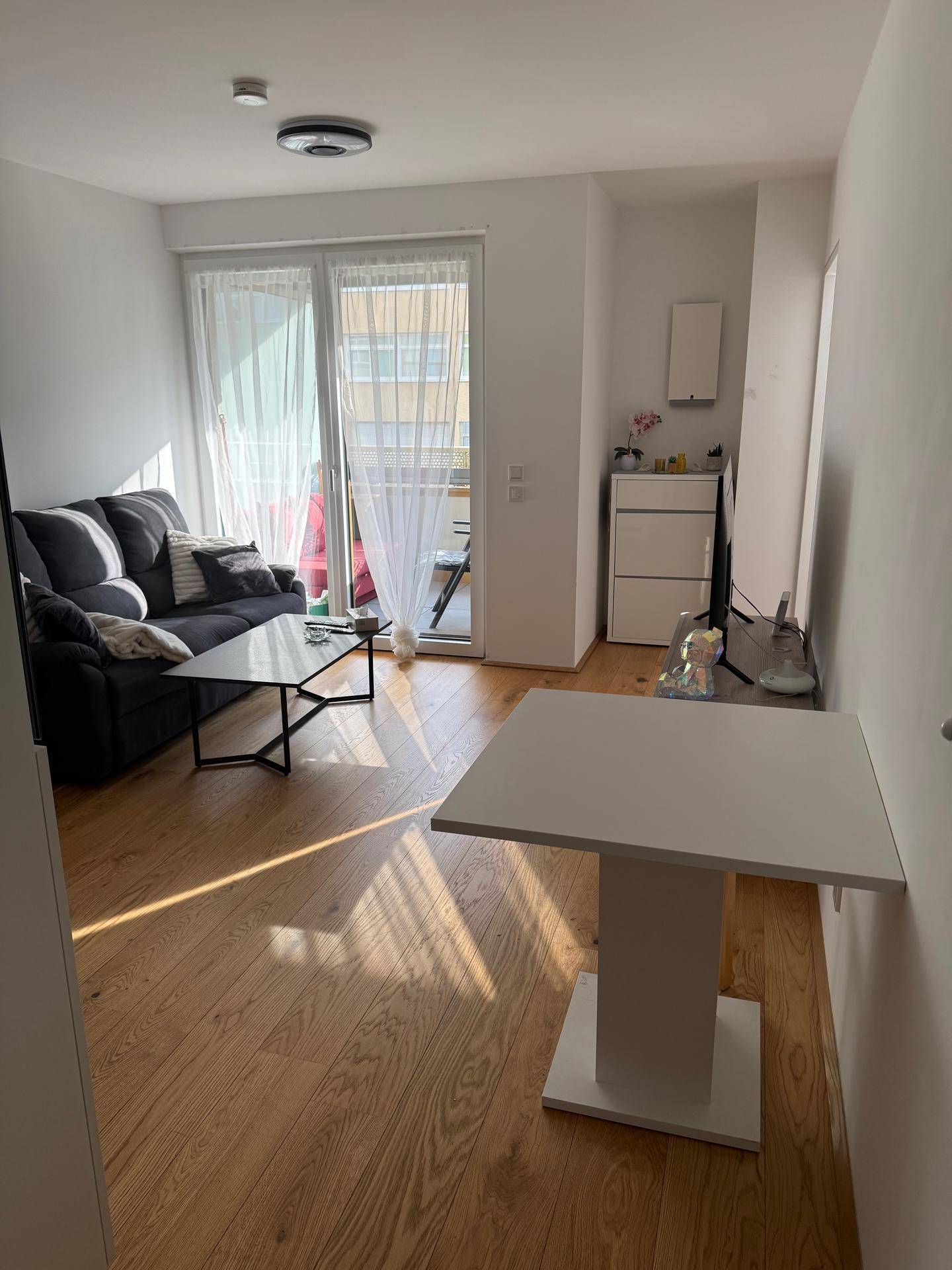 Lichtdurchflutetes Wohnzimmer mit Holzboden, Sofa und Zugang zu einem Balkon.