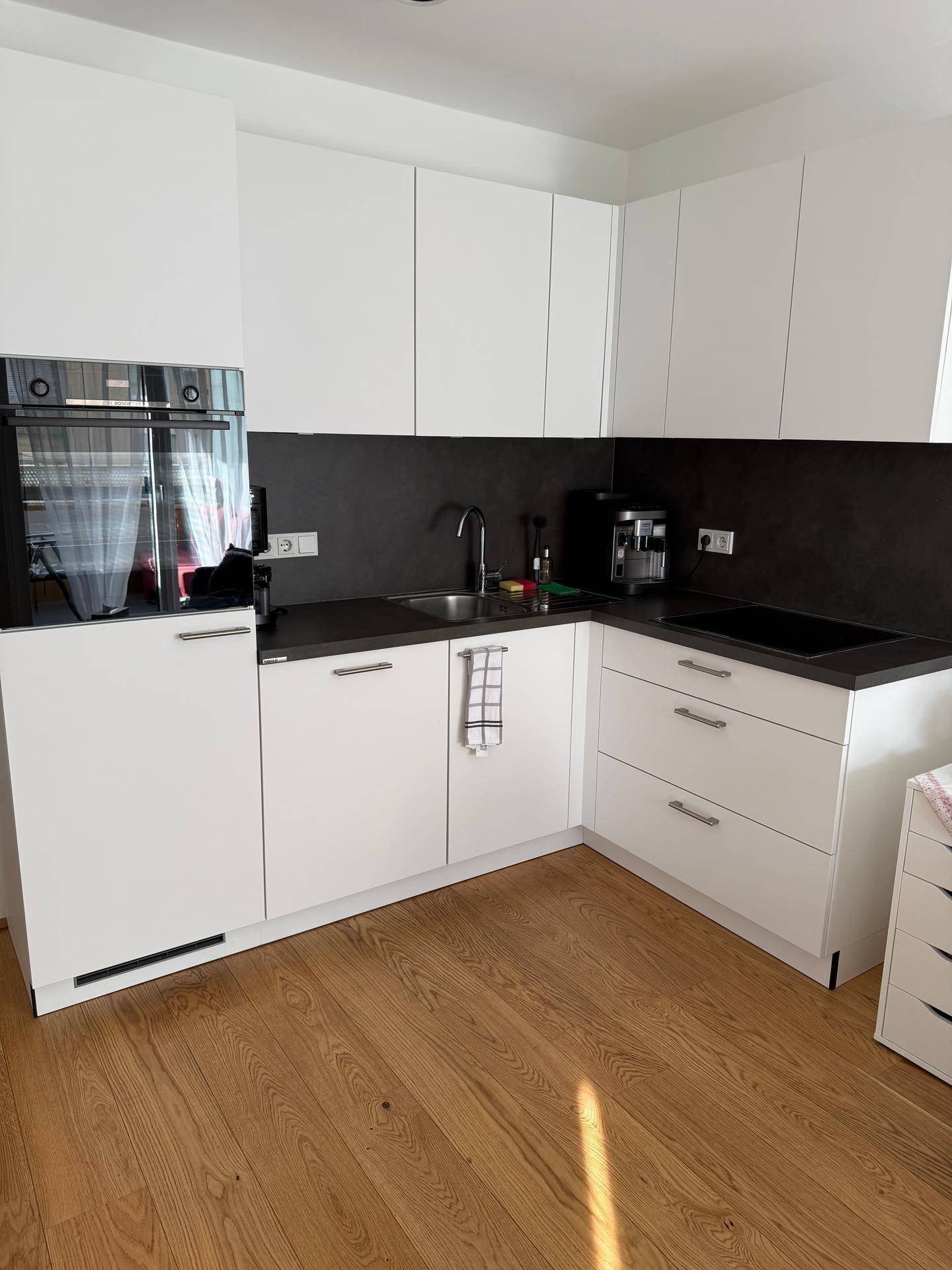 Moderne Einbauküche mit weißen Schränken, dunkler Arbeitsplatte und integrierten Geräten.