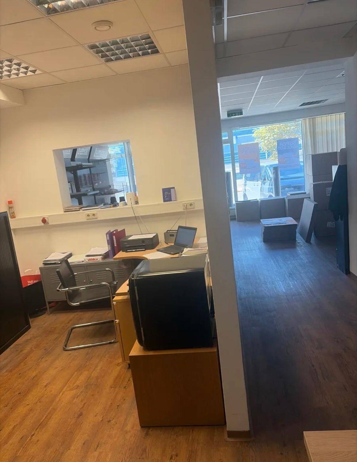 Bürobereich mit Schreibtisch, Drucker und Laptop, ausgestattet mit Laminatboden und einem Durchbruchfenster.
