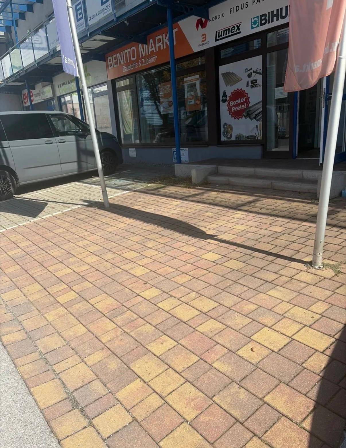 Außenansicht der Geschäftsfassade mit großen Schaufenstern und Eingangsbereich, davor ein gepflasterter Parkplatz.