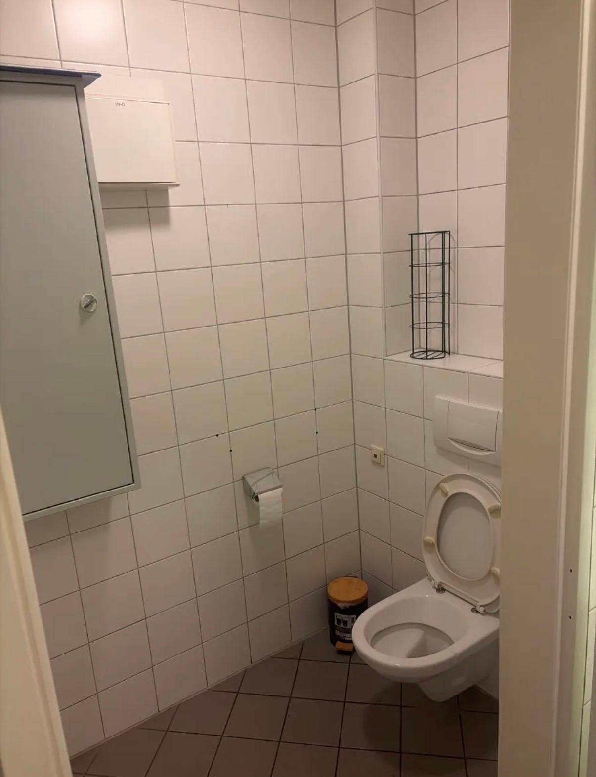 Kleiner Toilettenraum mit weißen Wand- und Bodenfliesen, ausgestattet mit WC und Spiegelschrank.
