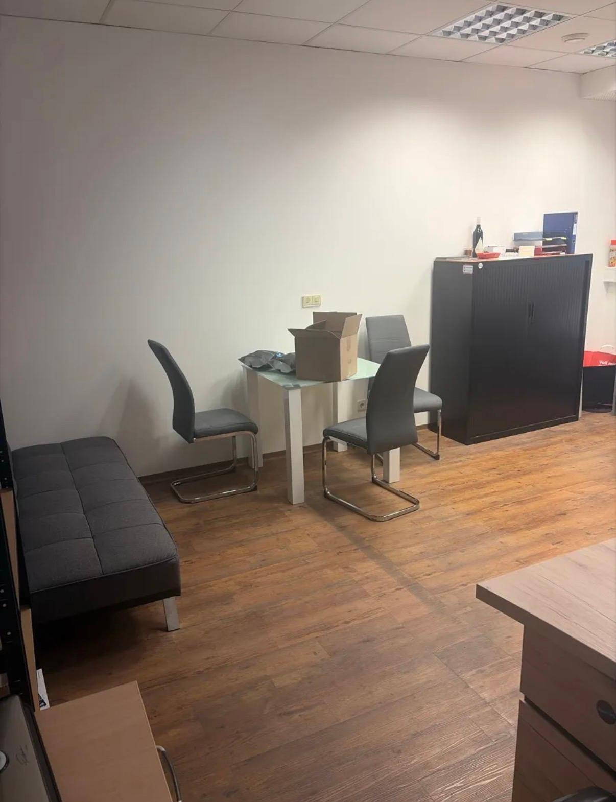 Sitzbereich mit kleinem Tisch, Stühlen und Sofa in einem offenen Raum mit Laminatboden und weißen Wänden.