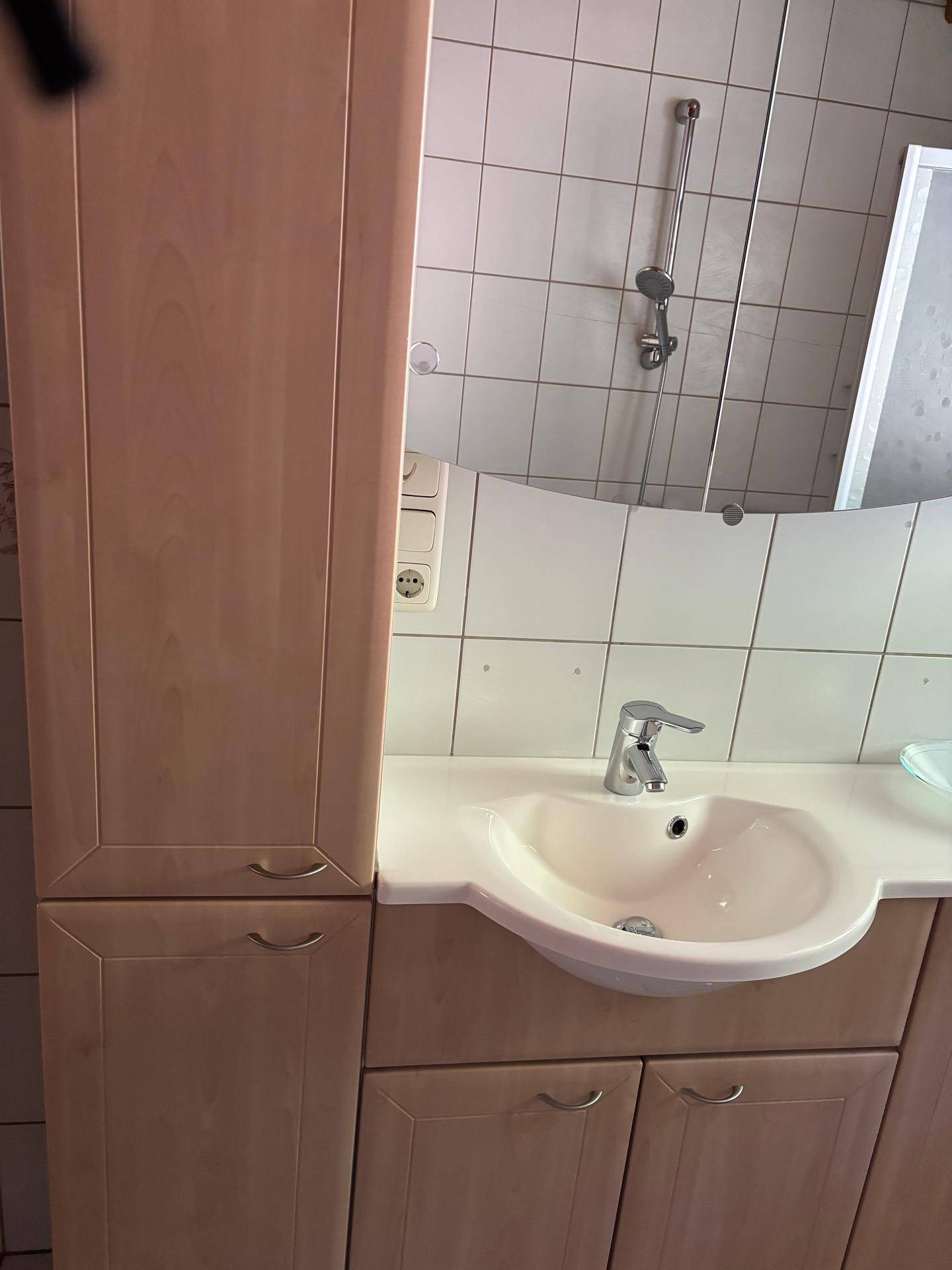 Nahaufnahme des Badezimmerwaschtisches mit Unterschrank und einem hohen Seitenschrank für Stauraum.