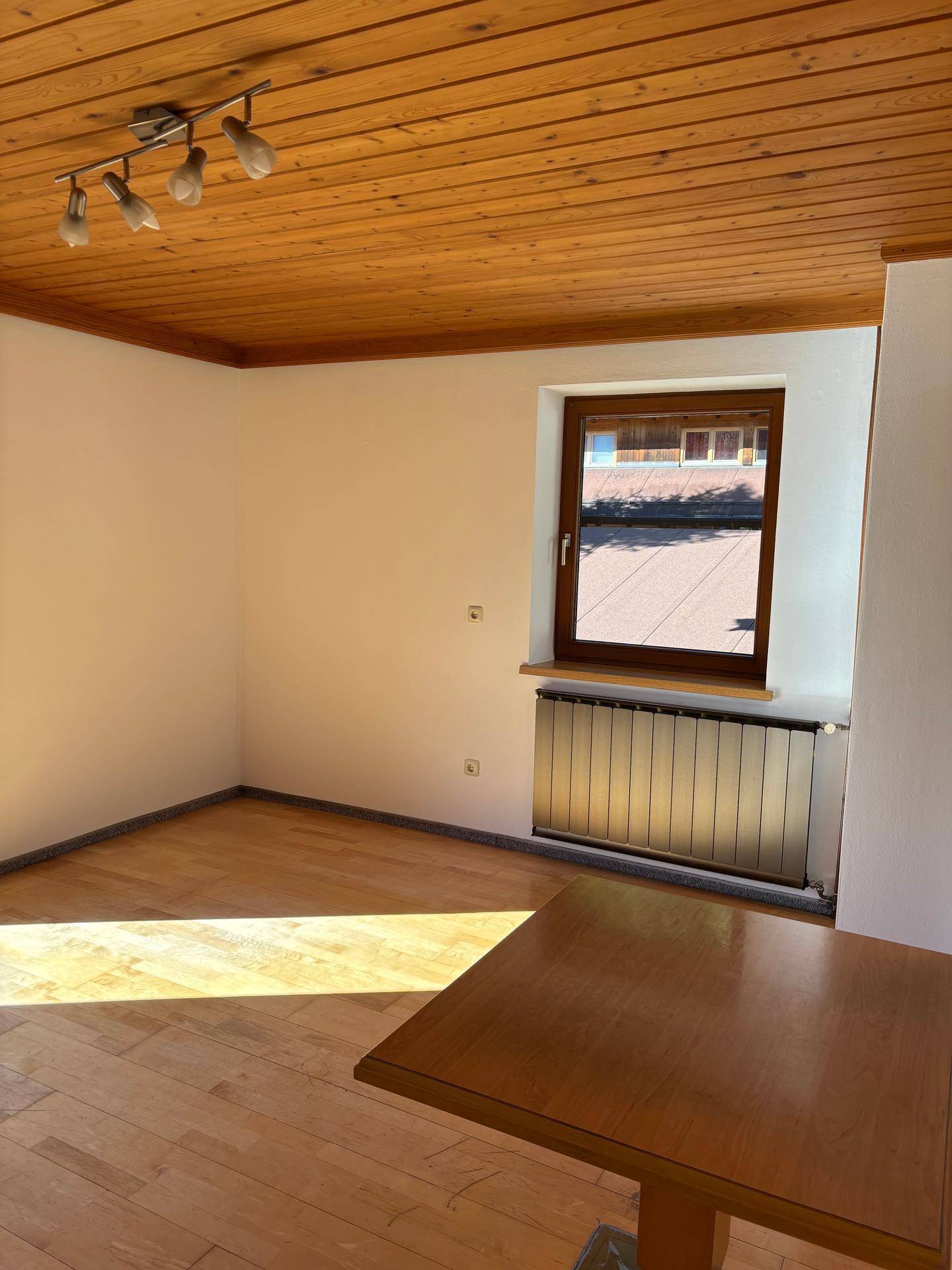 Geräumiges Zimmer mit Holzboden, Holzdecke und einem Fenster, das viel Tageslicht hereinlässt.