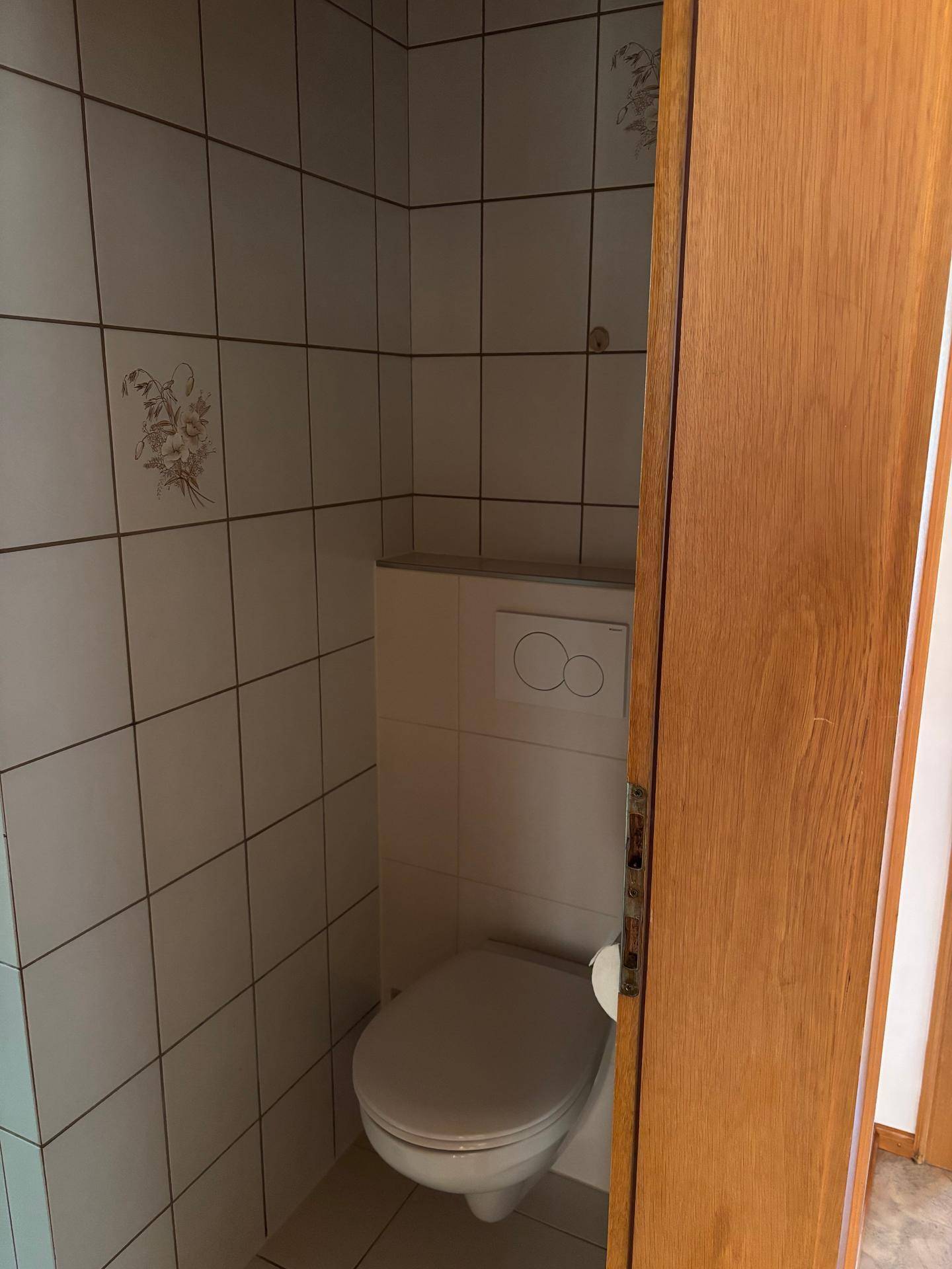 Separates WC mit weißen Fliesen, wandhängender Toilette und traditioneller Holzdecke.