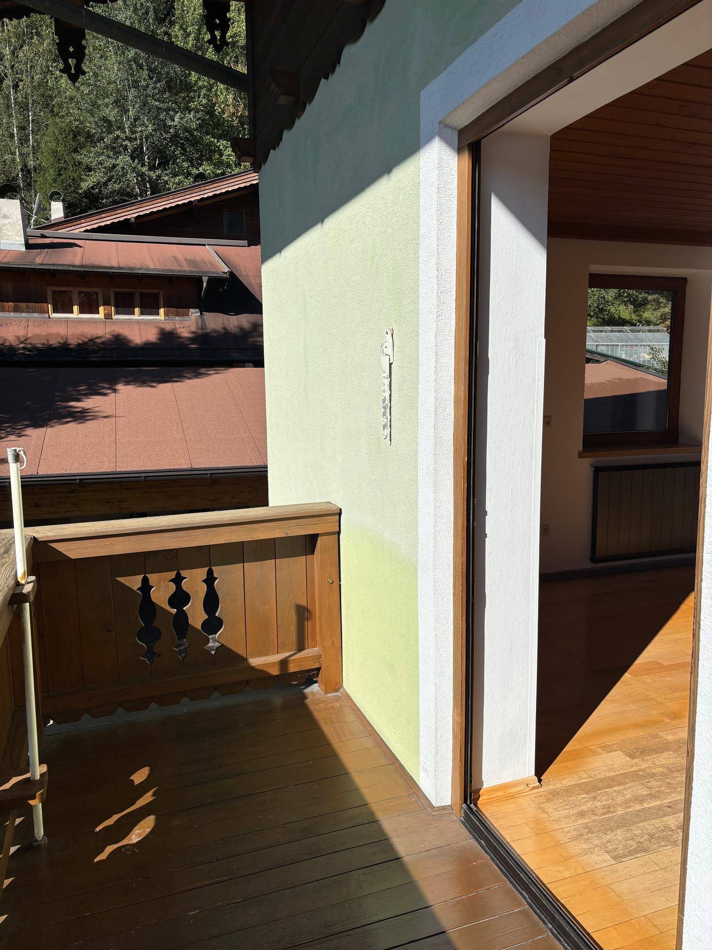 Gemütlicher Balkon mit Holzgeländer und Blick auf die umliegenden Häuser und grüne Bäume.