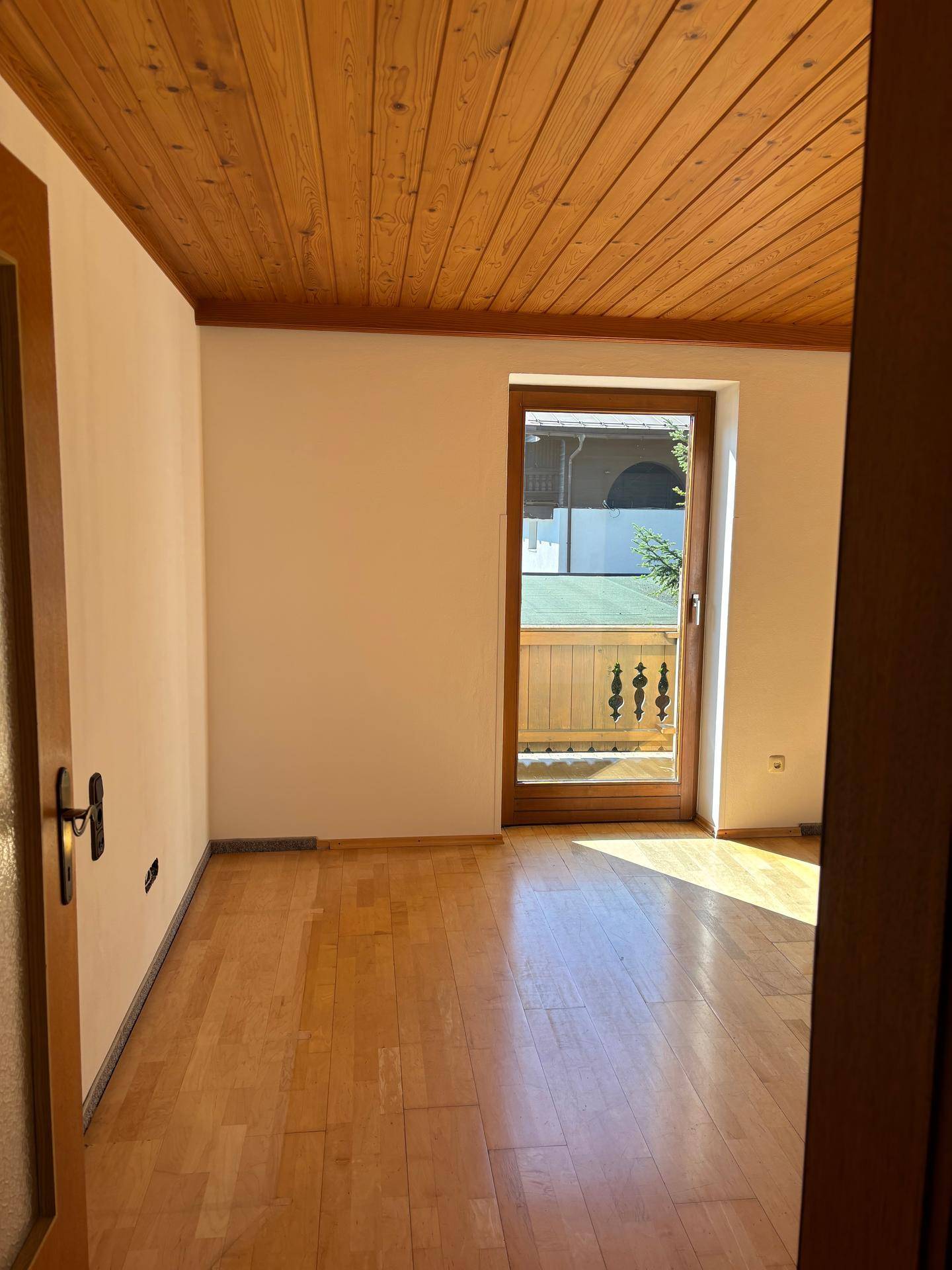 Helles Zimmer mit Holzboden, Holzdecke und direktem Zugang zu einem charmanten Balkon.
