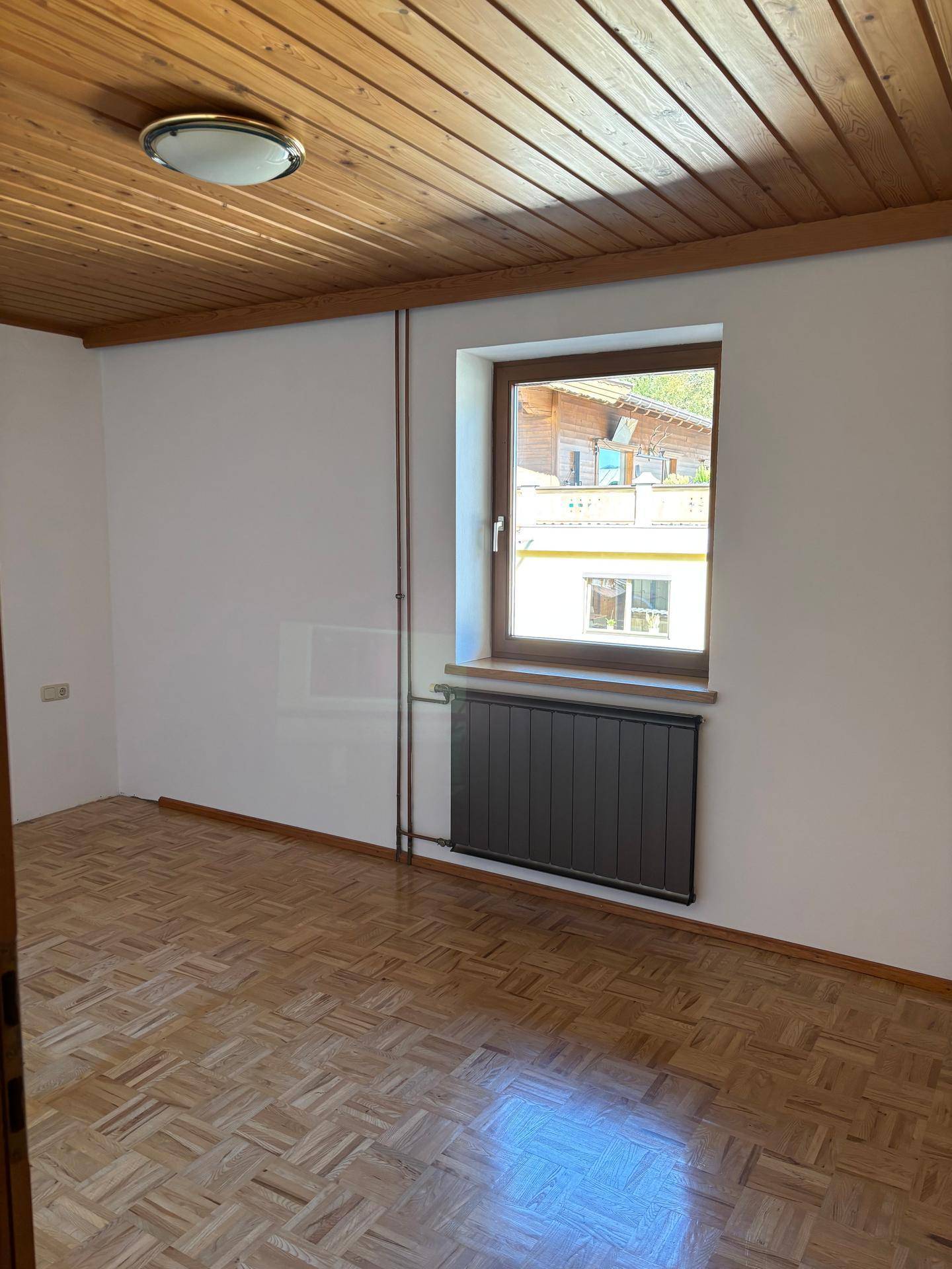 Leeres Schlafzimmer mit traditioneller Holzdecke, Parkettboden und einem Fenster mit Blick nach draußen.