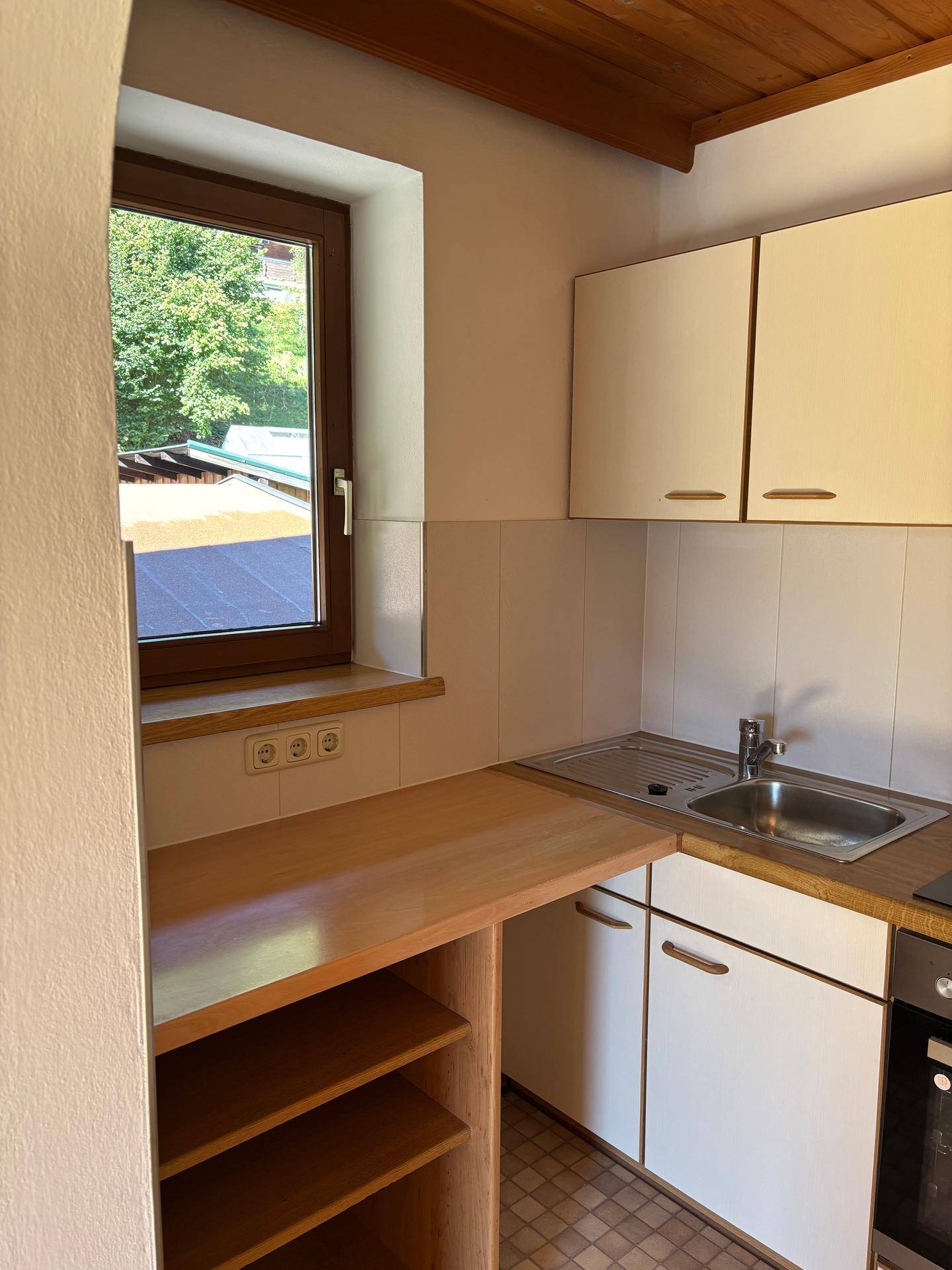 Helle Küchenzeile mit Fenster, weißen Schränken, Holzarbeitsplatte und Spülbecken.