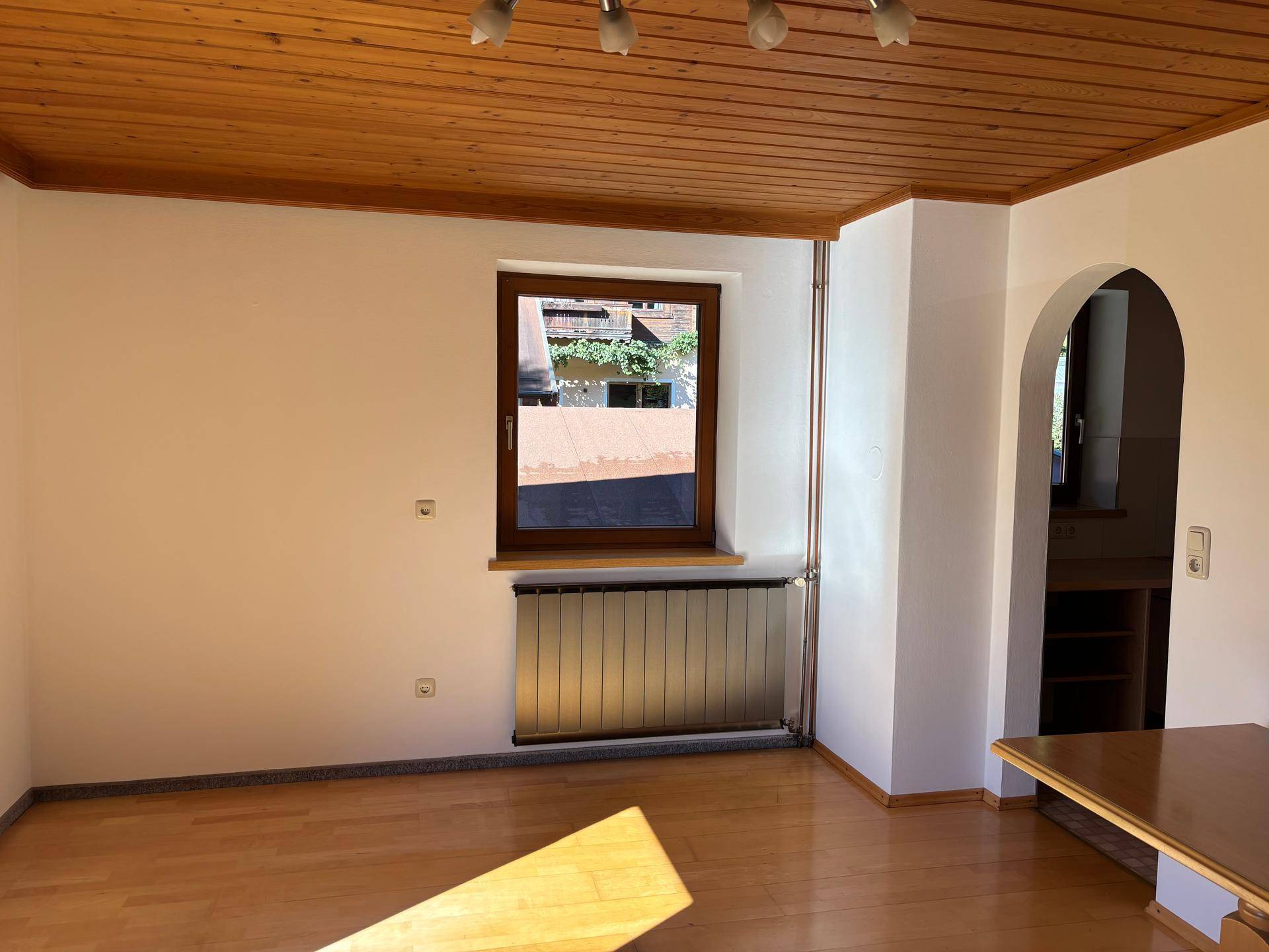Heller Wohnbereich mit Holzboden, Holzdecke und einem Rundbogen, der zu einem weiteren Raum führt.