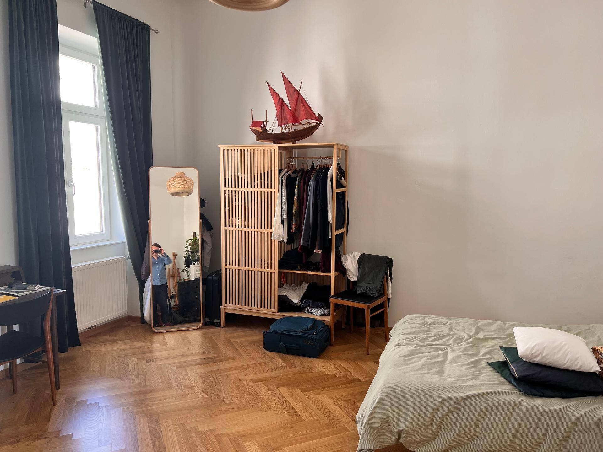 Schlafzimmer mit Fischgrätparkett, einem Bett und einem offenen Holzschrank.