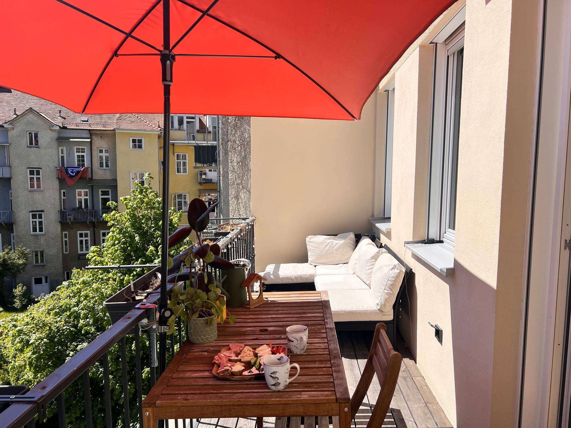 Geräumiger Balkon mit orangefarbenem Sonnenschirm, Esstisch und bequemer Lounge-Sitzgruppe.