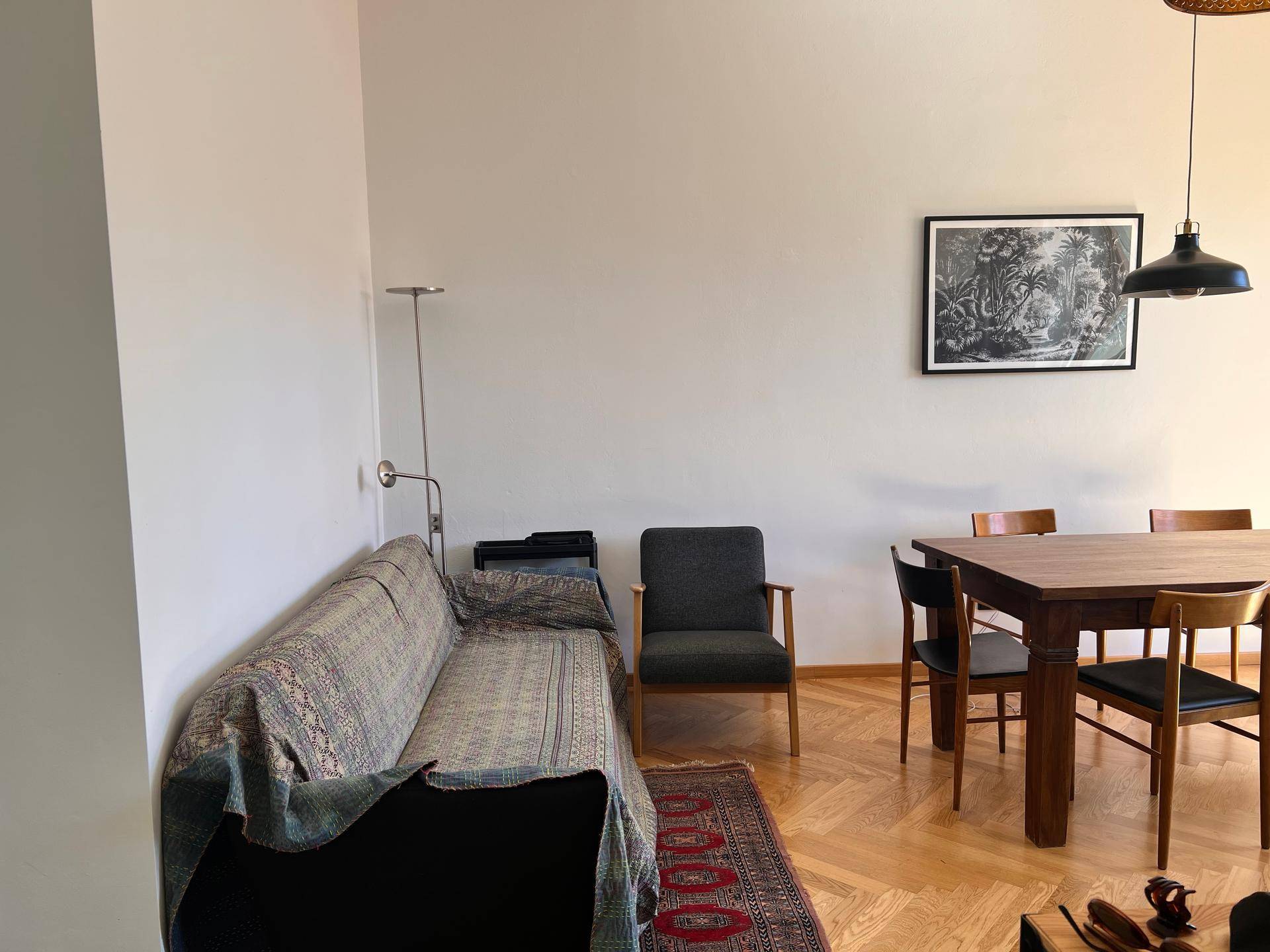 Gemütlicher Wohnbereich mit Sofa, Sessel und klassischem Fischgrätparkettboden.