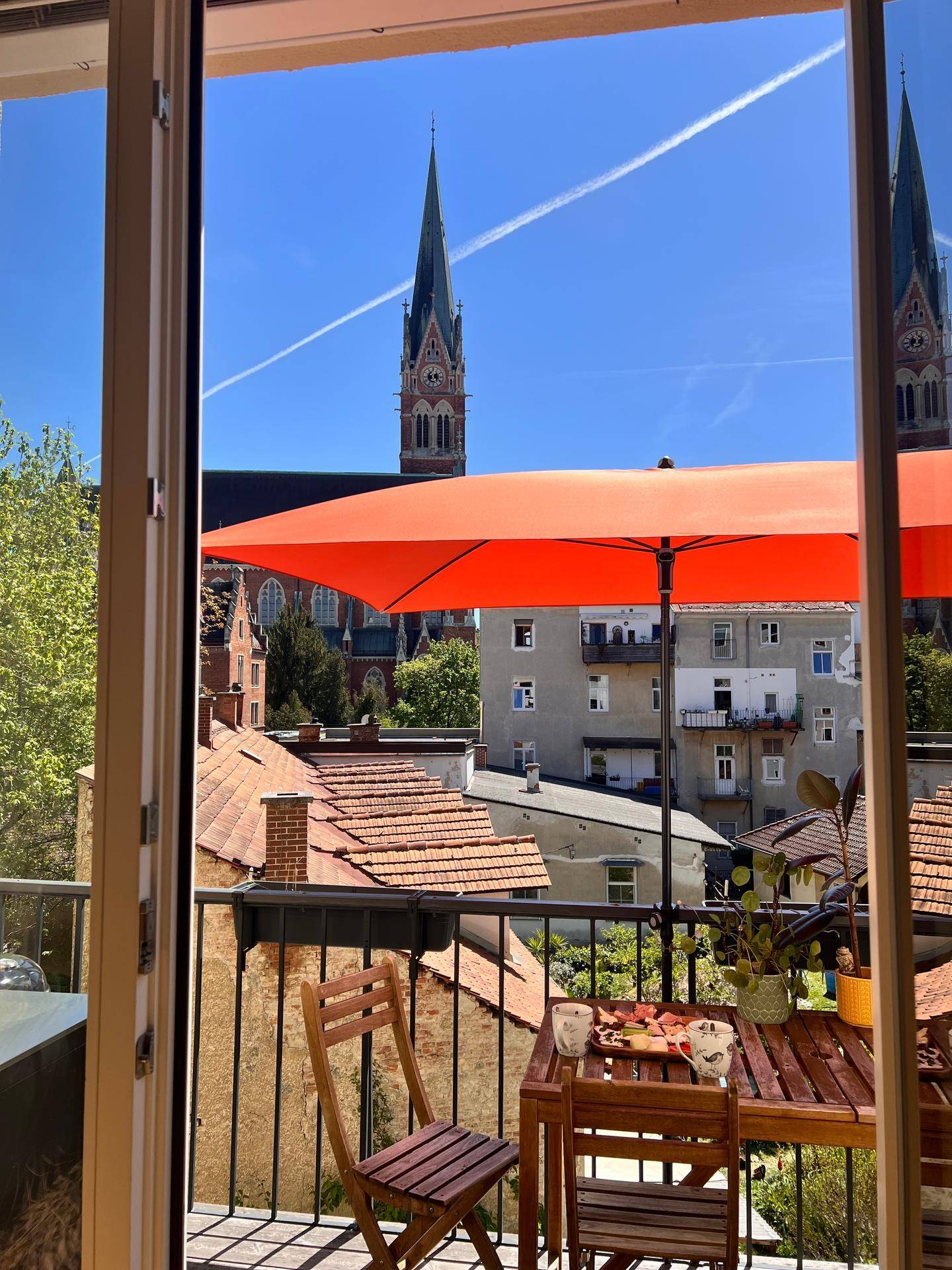 Balkon mit Stadtblick und einem markanten Kirchturm unter blauem Himmel.