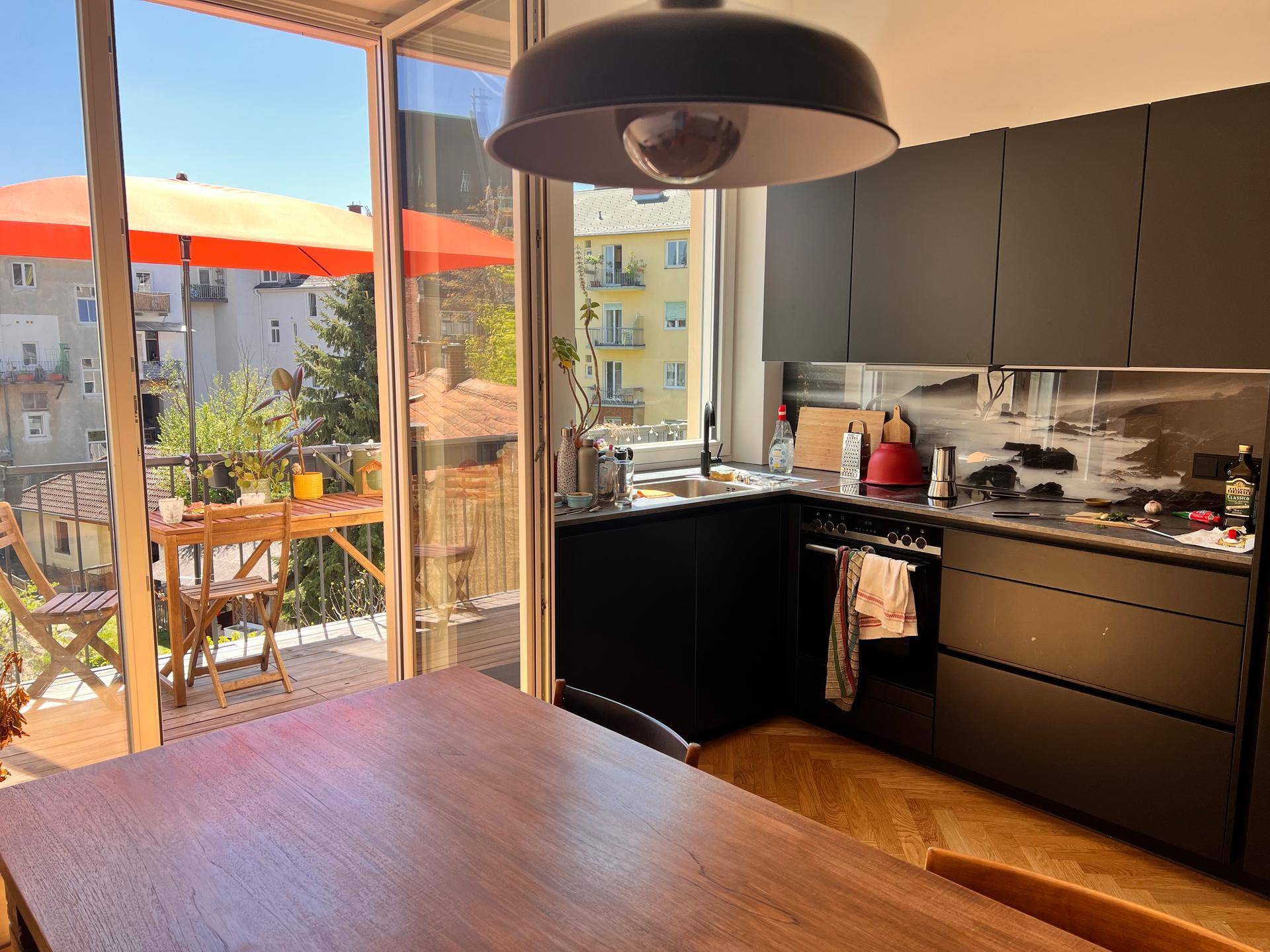 Moderne Küche mit dunklen Schränken und Essbereich, mit Zugang zu einem sonnigen Balkon.