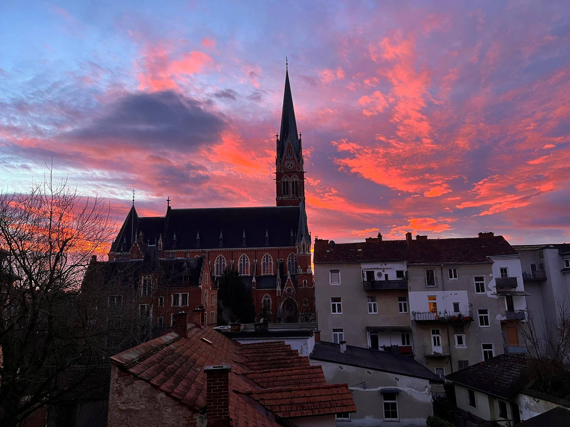Dramatischer Sonnenuntergang über einer historischen Kirche und den Dächern der Stadt.