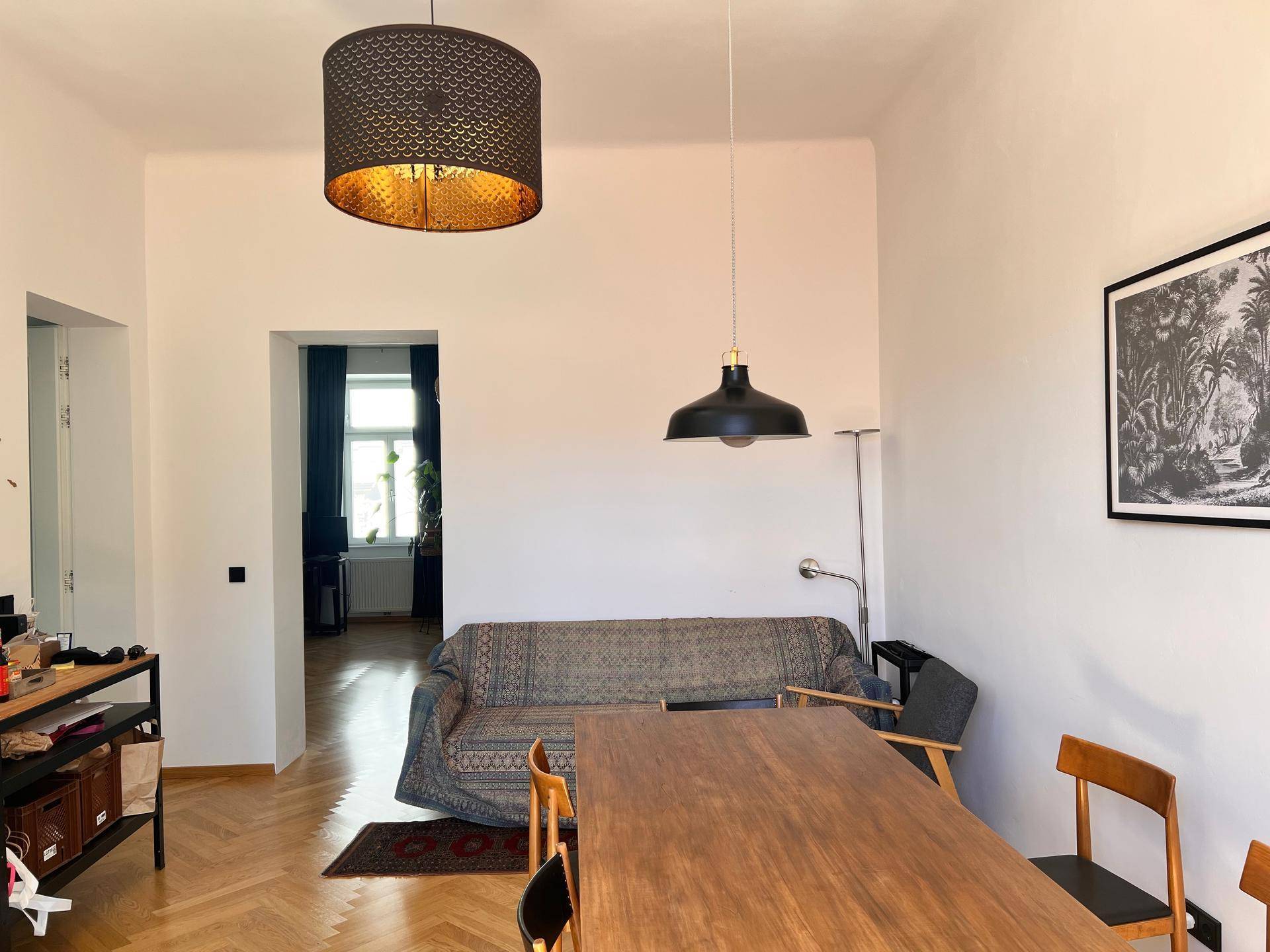 Geräumiger Wohn-Essbereich mit Holztisch, Sofa und klassischem Fischgrätparkettboden.