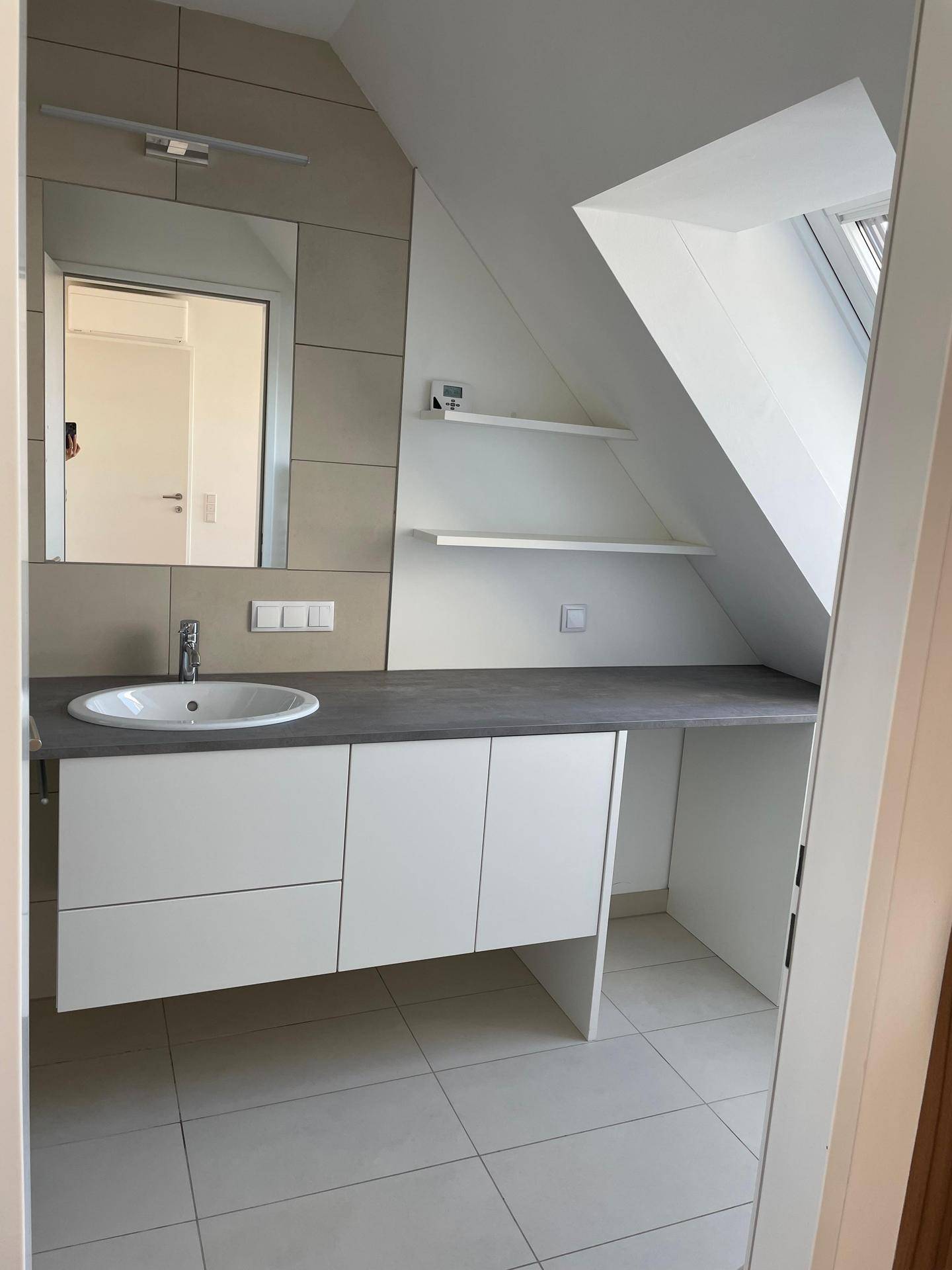 Modernes Badezimmer mit Waschtisch, Spiegel und Dachfenster für natürliches Licht und Belüftung.