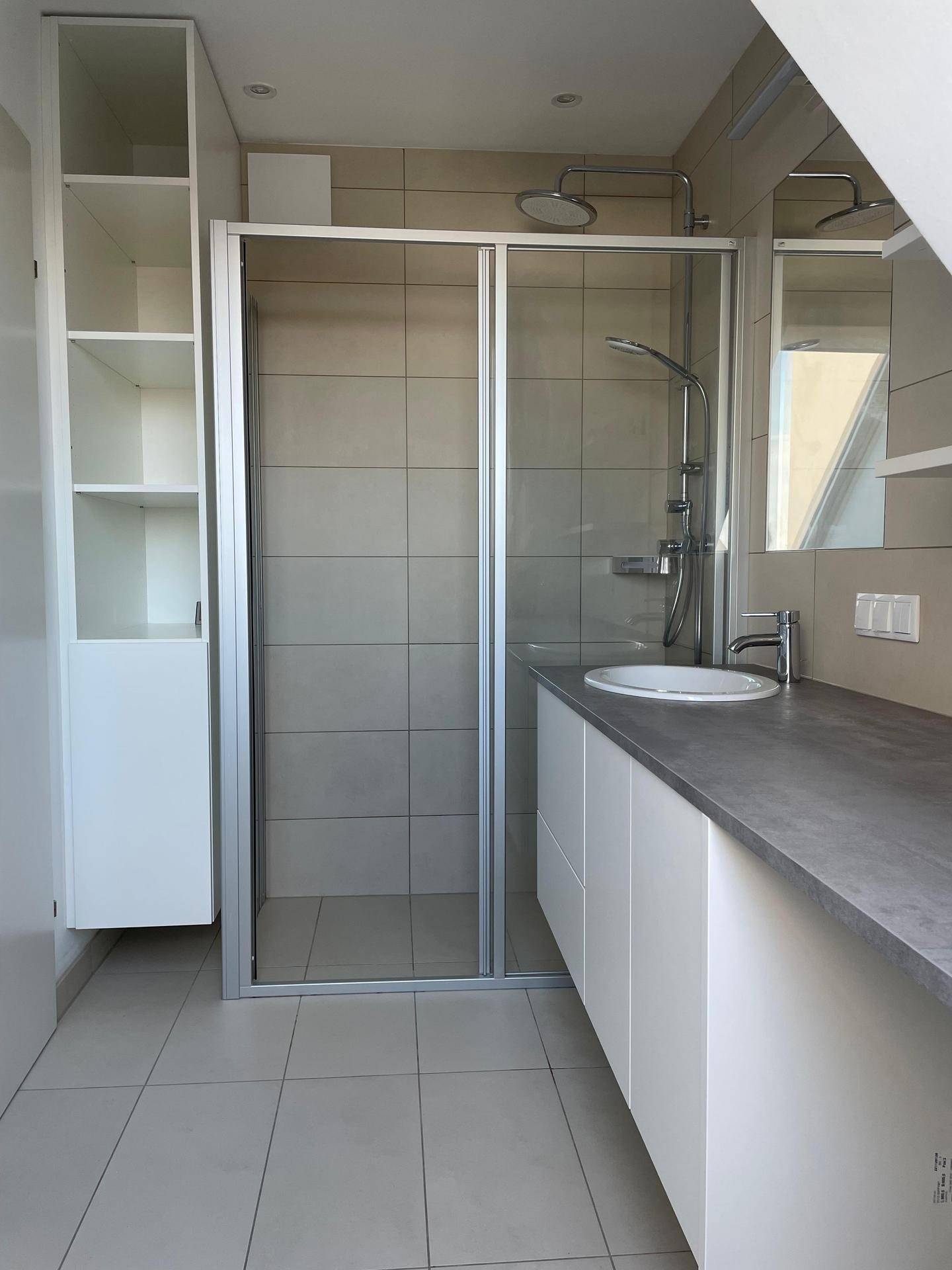 Modernes Badezimmer mit Duschkabine, Waschtisch und großformatigen Fliesen an Wänden und Boden.