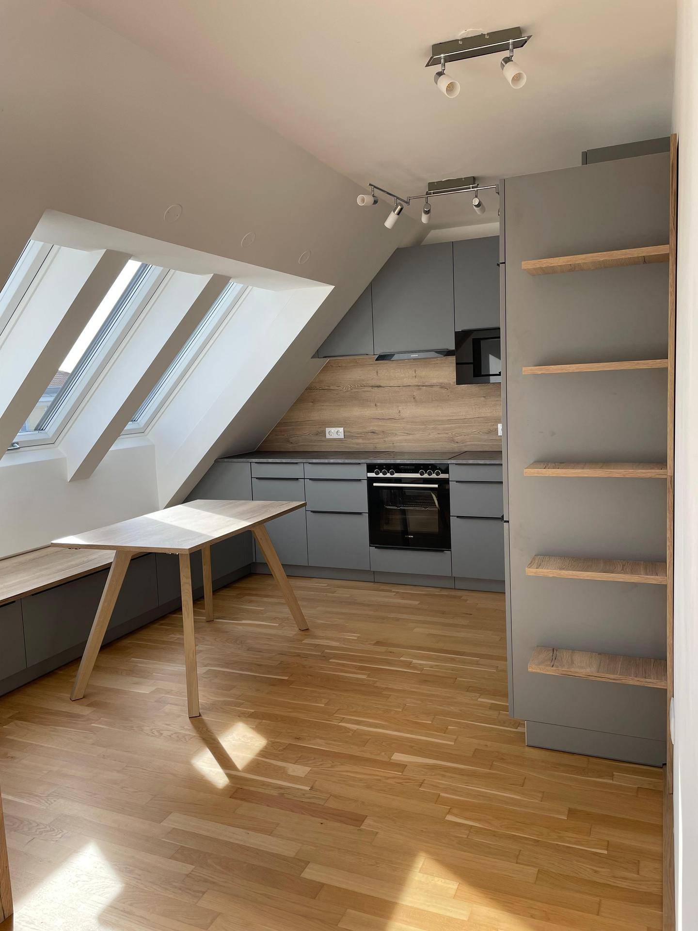 Moderne Küche im Dachgeschoss mit grauen Schränken, Holzboden und viel Tageslicht durch die Dachfenster.
